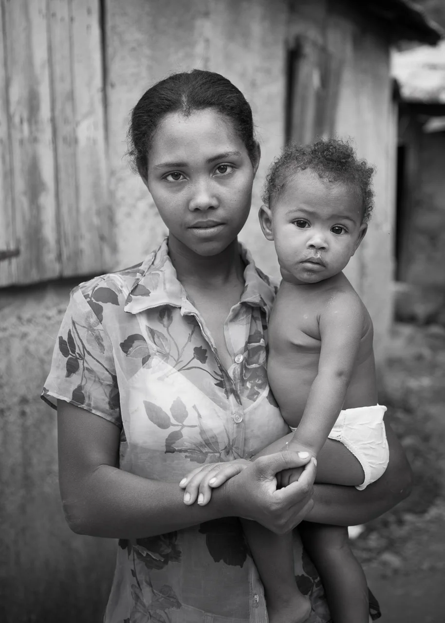 A young woman holding a small child outdoors, both looking at the camera, in black and white.
