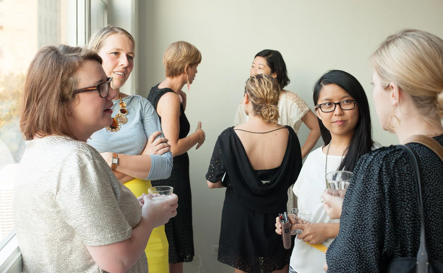 Group of women having a conversation at a social gathering indoors near a window.