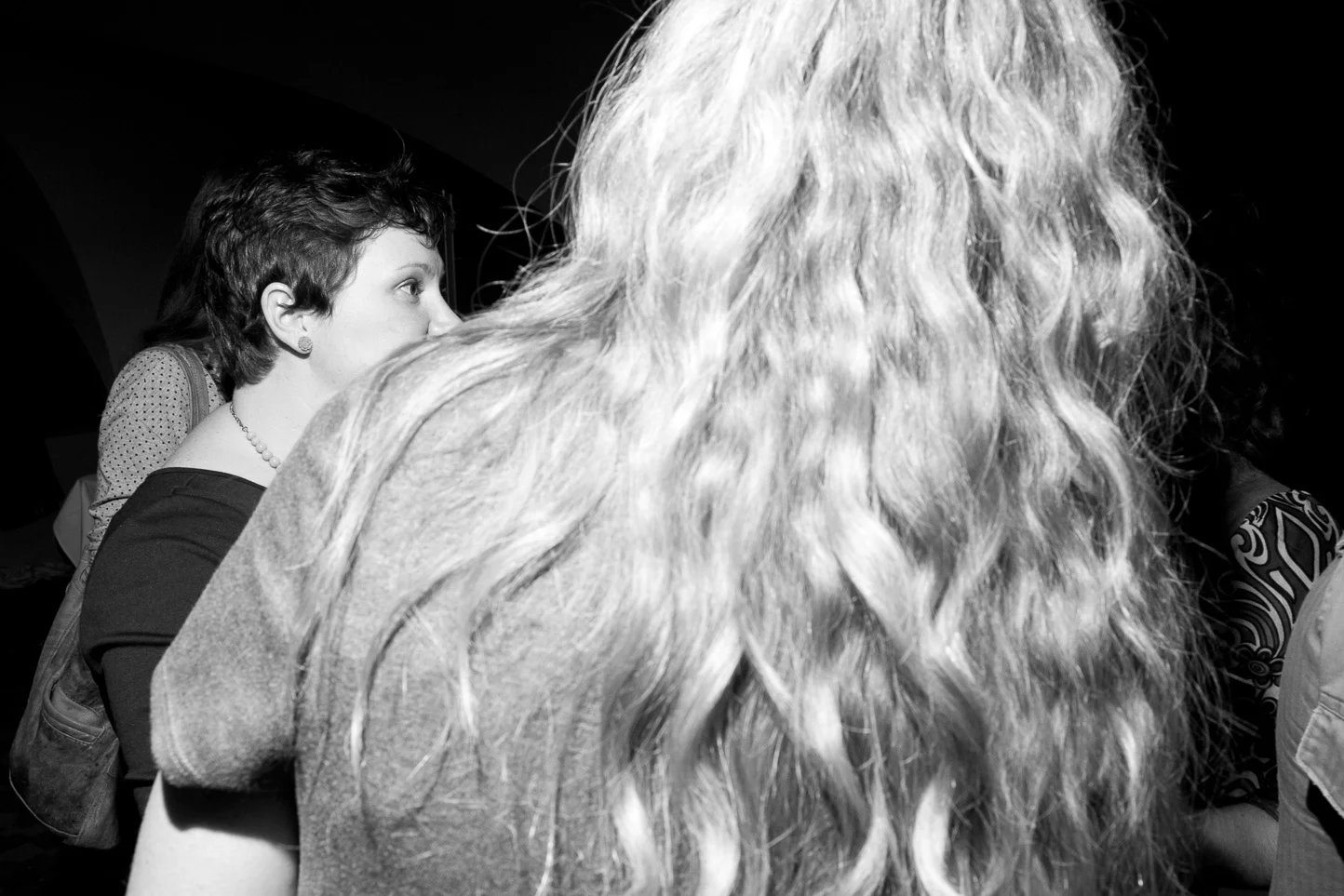 Black and white photo of two women sitting in profile, one with short dark hair and the other with long, wavy light hair, in a dimly lit room.