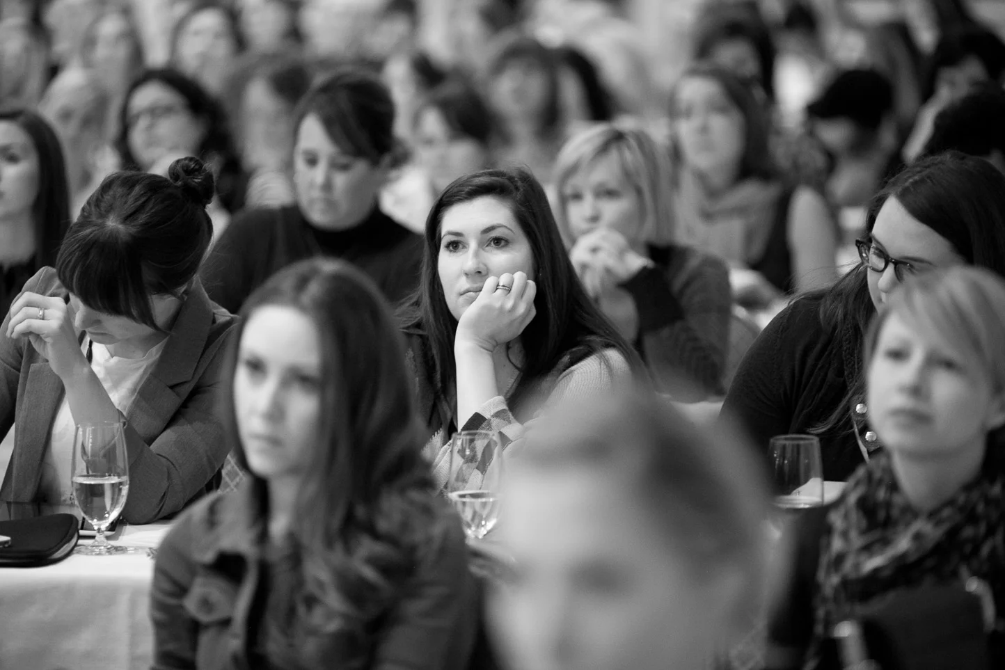 Black and white photo of a large group of women attending a conference or seminar, seated at a long table, listening attentively.