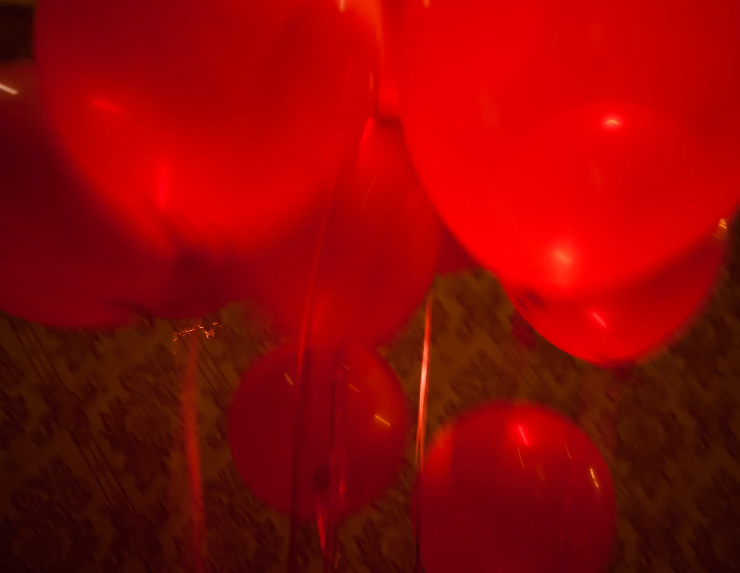 Close-up of red balloons with reflections, seen from below, with a wooden floor beneath.