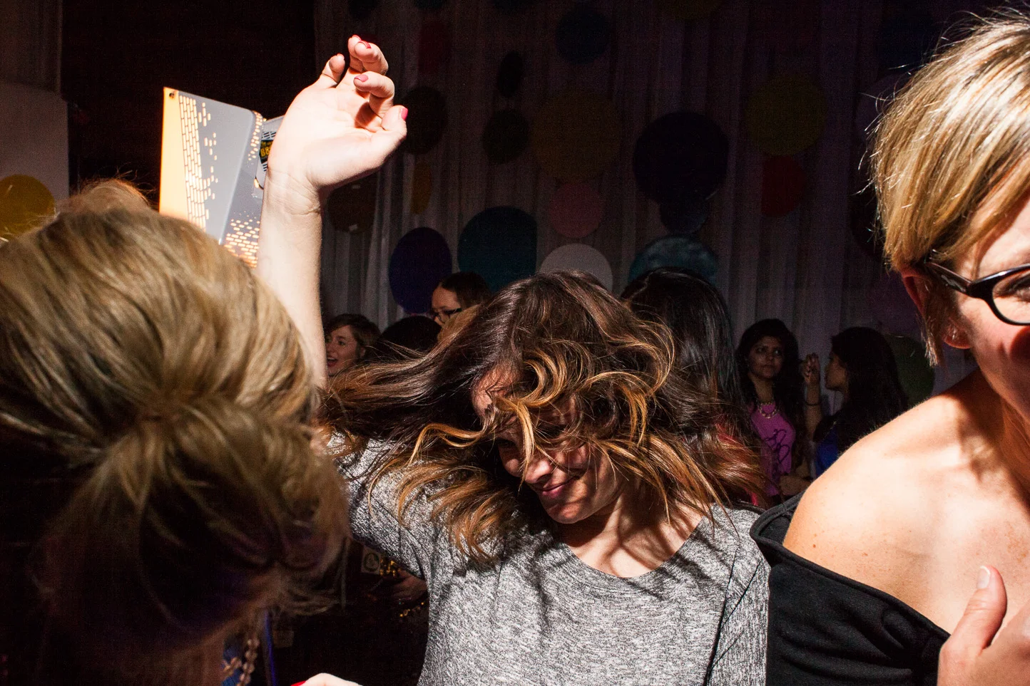 Group of women dancing and enjoying themselves at a party or celebration, with colorful balloons in the background.
