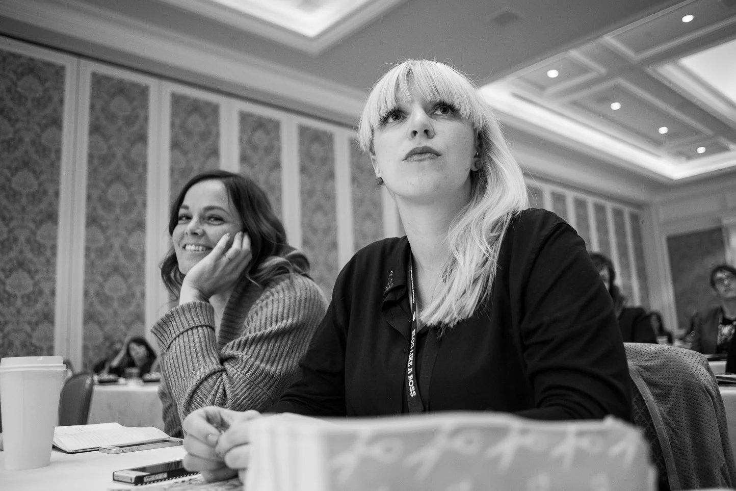 Black and white photo of women sitting at conference table in a formal setting, attending a professional event or meeting.