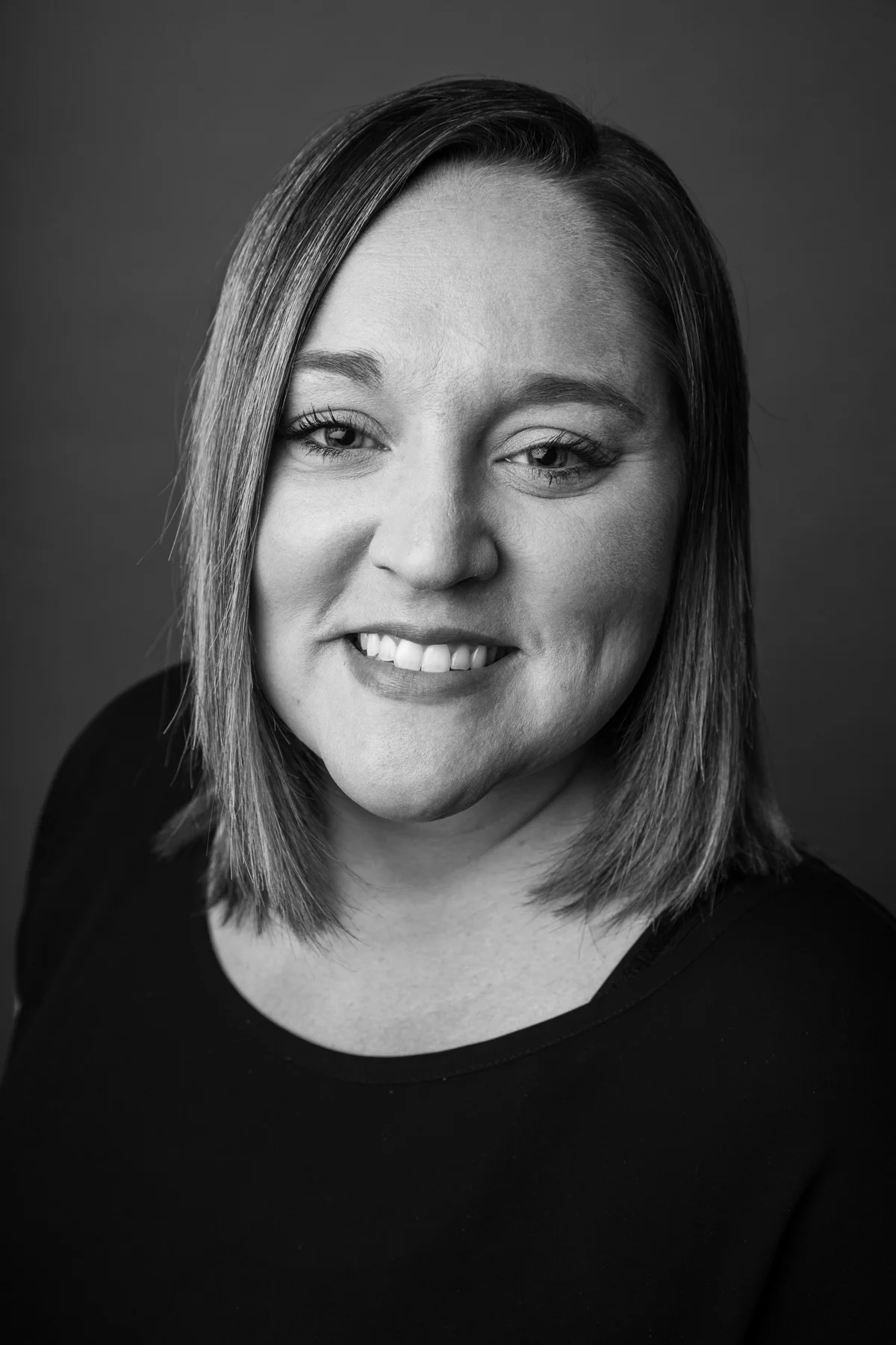 Black and white portrait of a woman with shoulder-length hair, smiling, wearing a dark top.