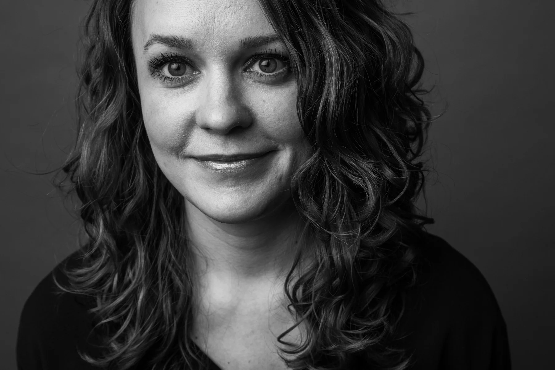 Black and white portrait of a woman with wavy hair, smiling gently, looking directly at the camera.