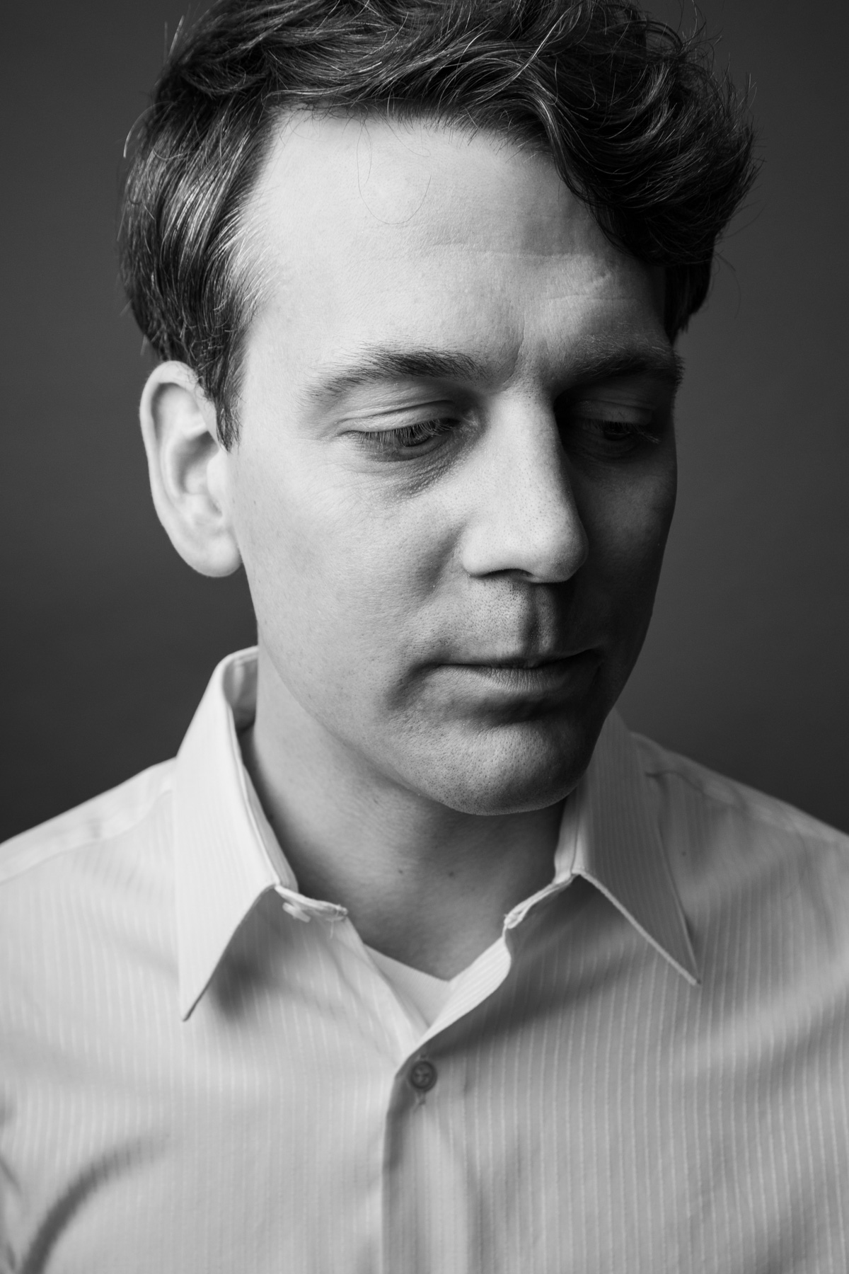 Black and white portrait of a young man with short, dark hair, wearing a collared shirt, looking downward with a contemplative expression.