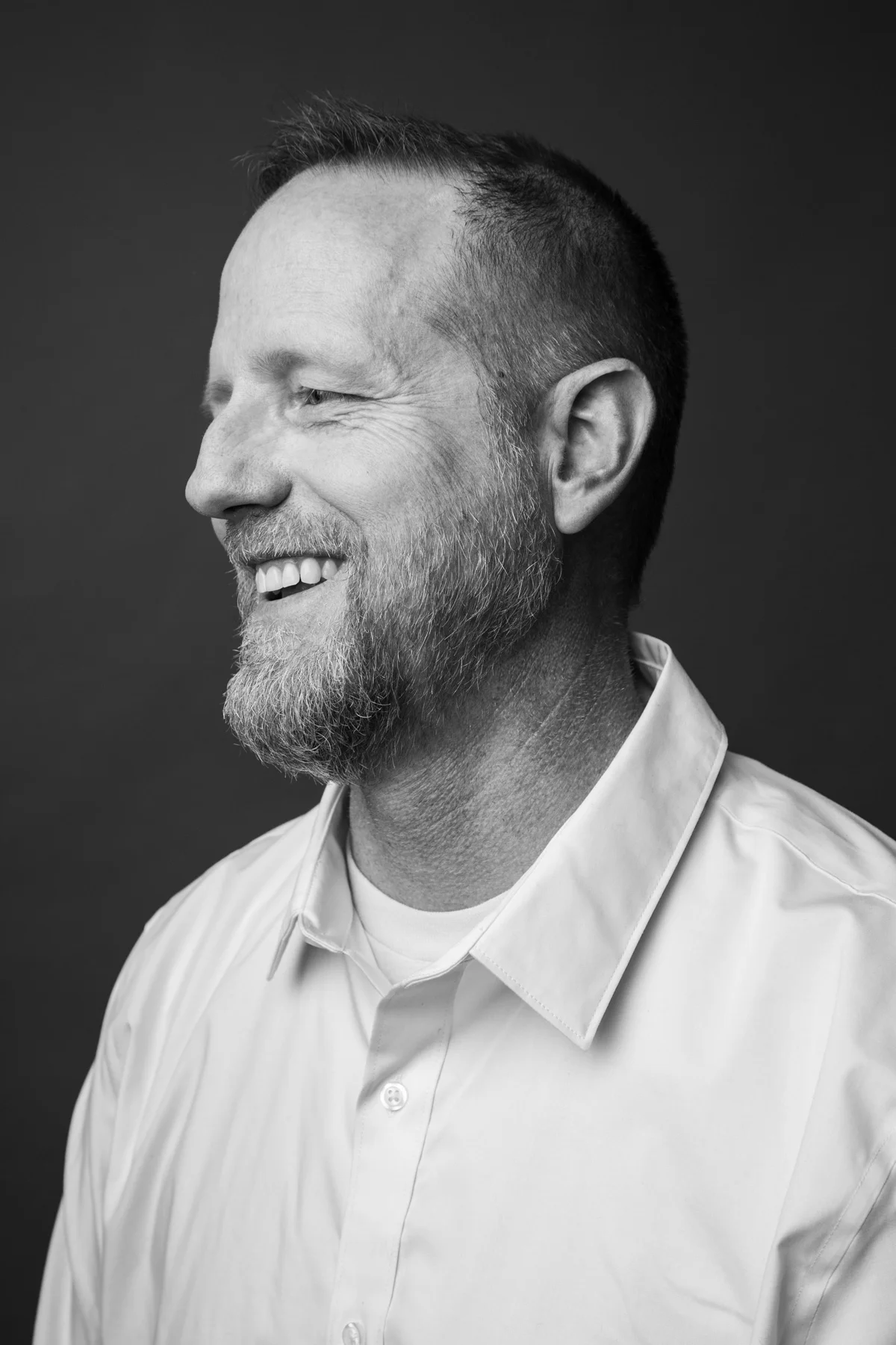 Black and white portrait of a smiling man with a beard, wearing a collared shirt, facing left.