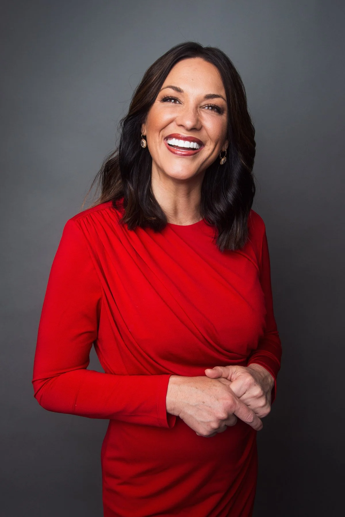 A smiling woman in a red dress with shoulder-length dark hair, posing against a gray background.
