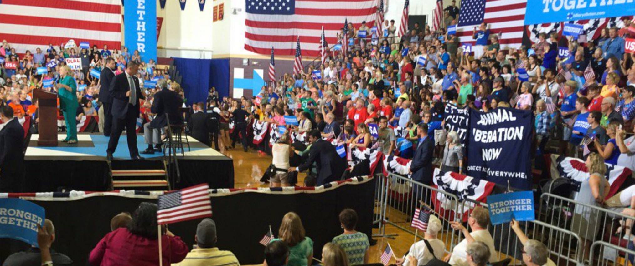 DxE activists unfurl a banner during a Hillary Clinton rally in Des Moines, IA