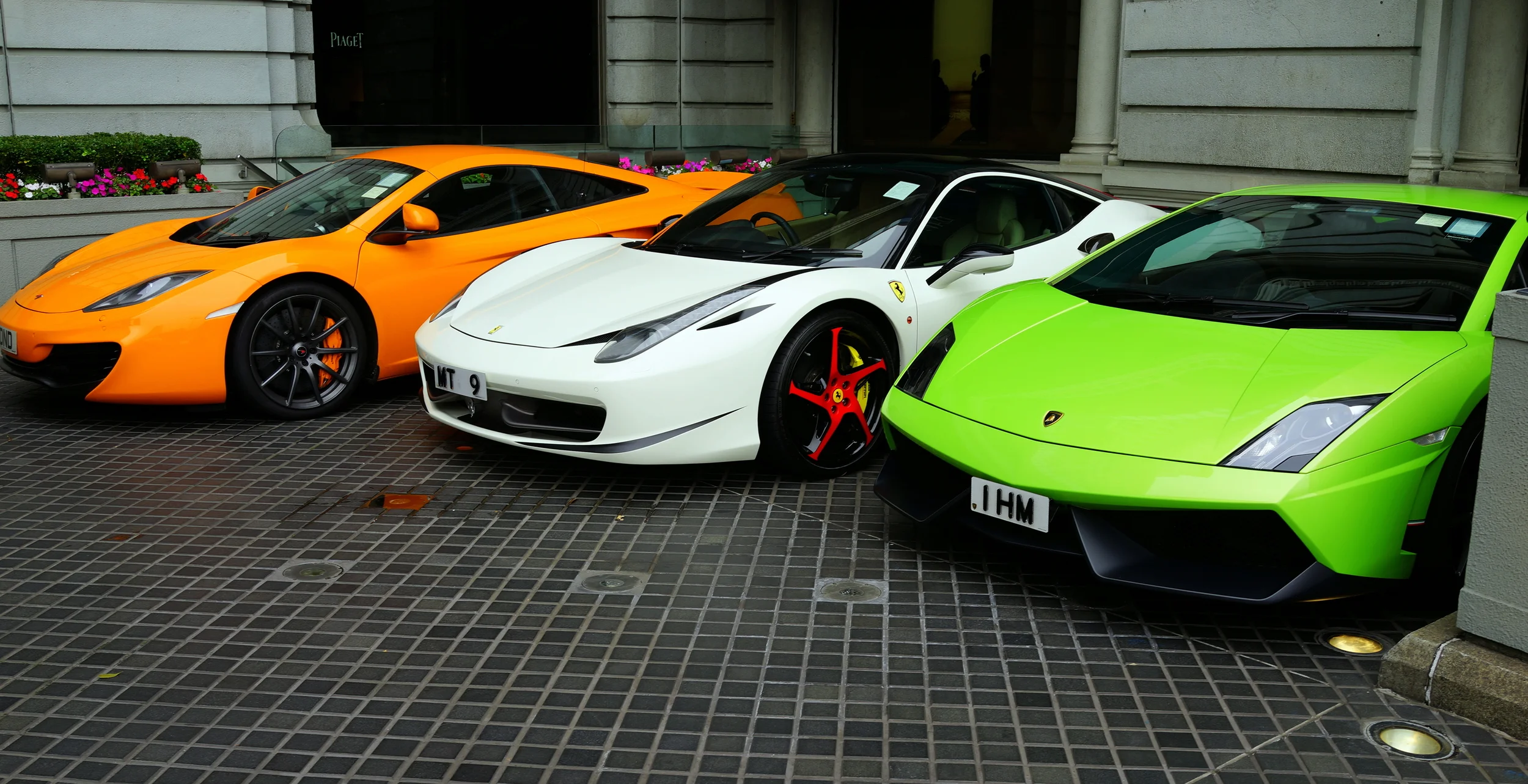 An orange McLaren, a white Ferrari and a green Lamborghini parked at the Peninsula Hotel