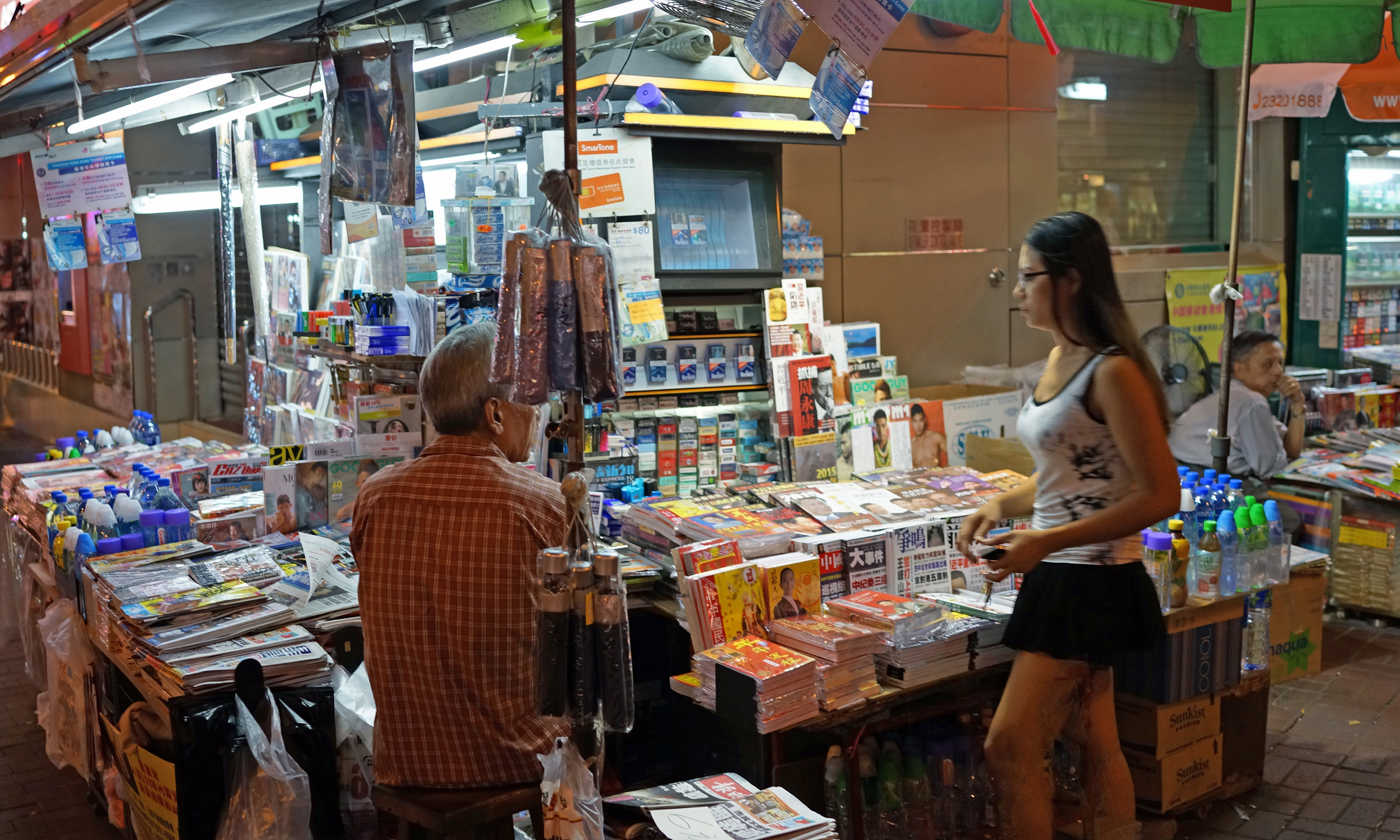 A typical newspaper stall - the old bloke is probably granddad and the young lady his grand daughter, they are sat there probably 350 days a year, 15 hours a day in all types of weather.