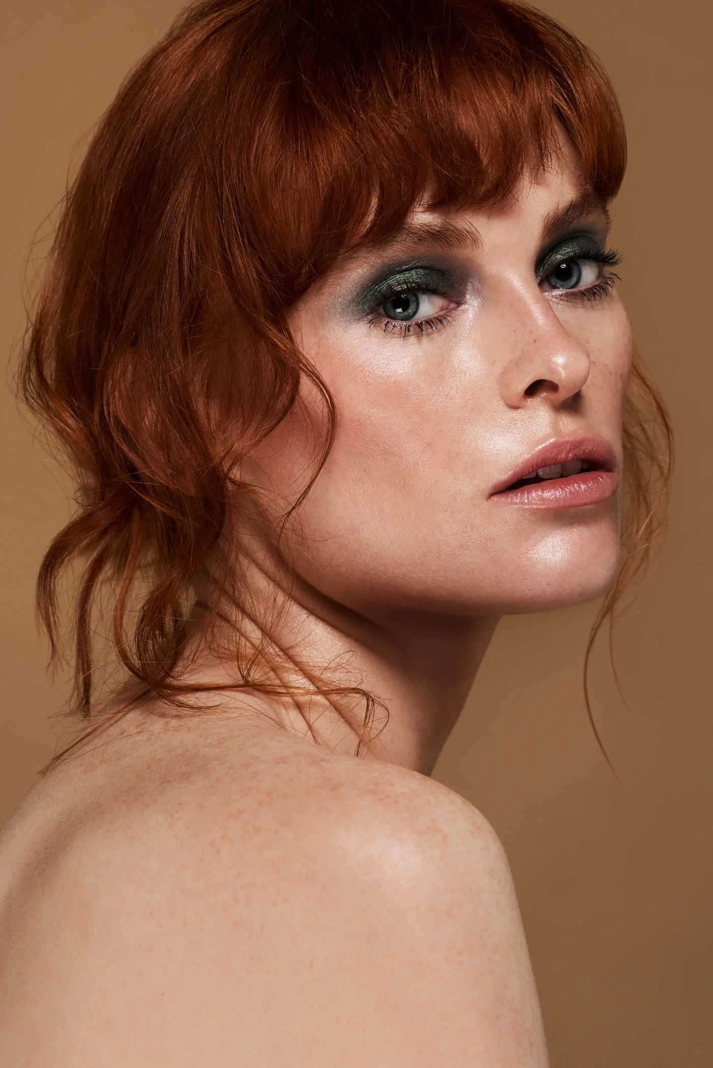 freckled beauty model with ginger hair and green eyeshadow on a warm brown backdrop