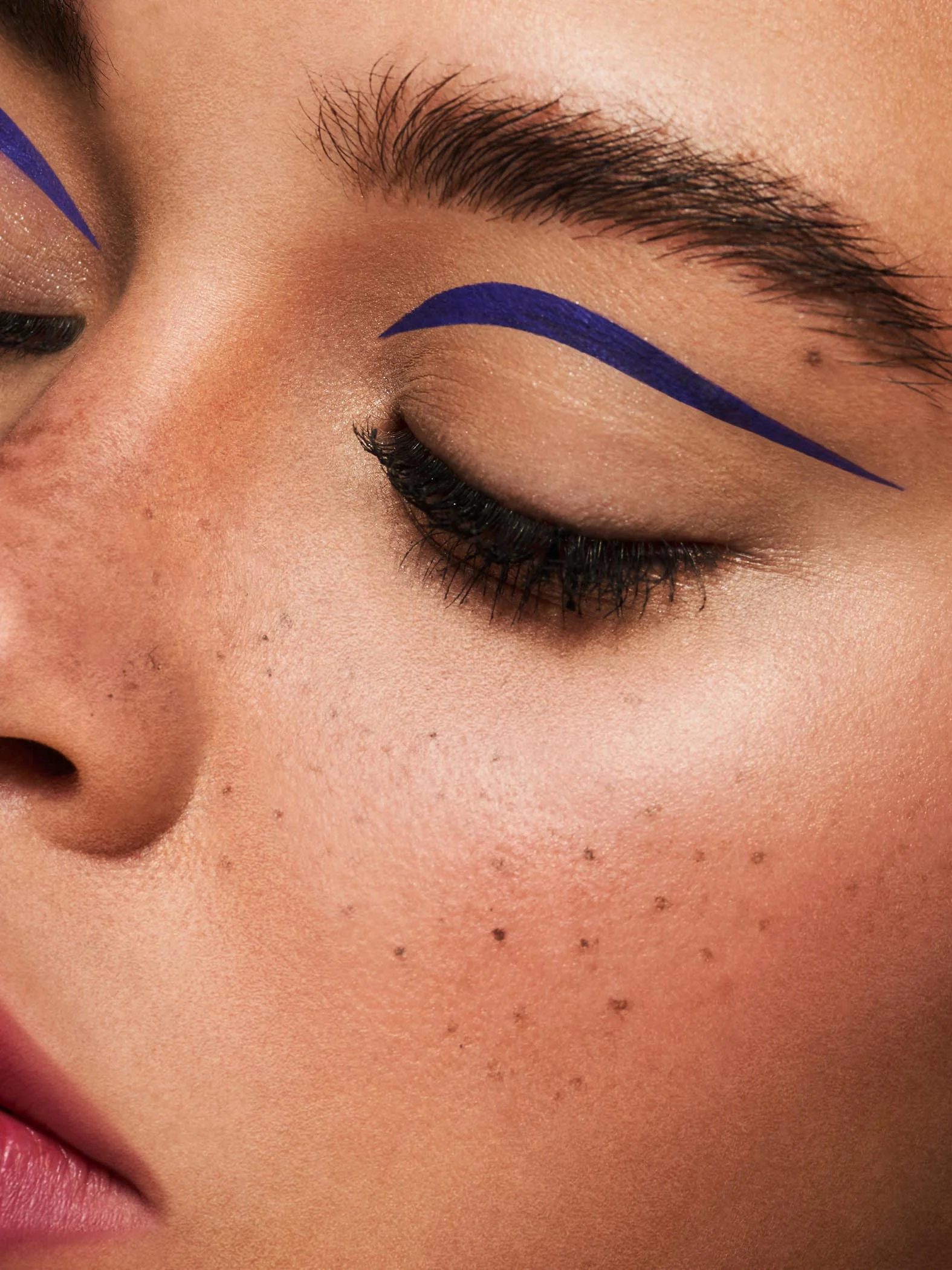 close up macro beauty shoot featuring mixed race beauty model with faux freckles and creative purple eyeliner