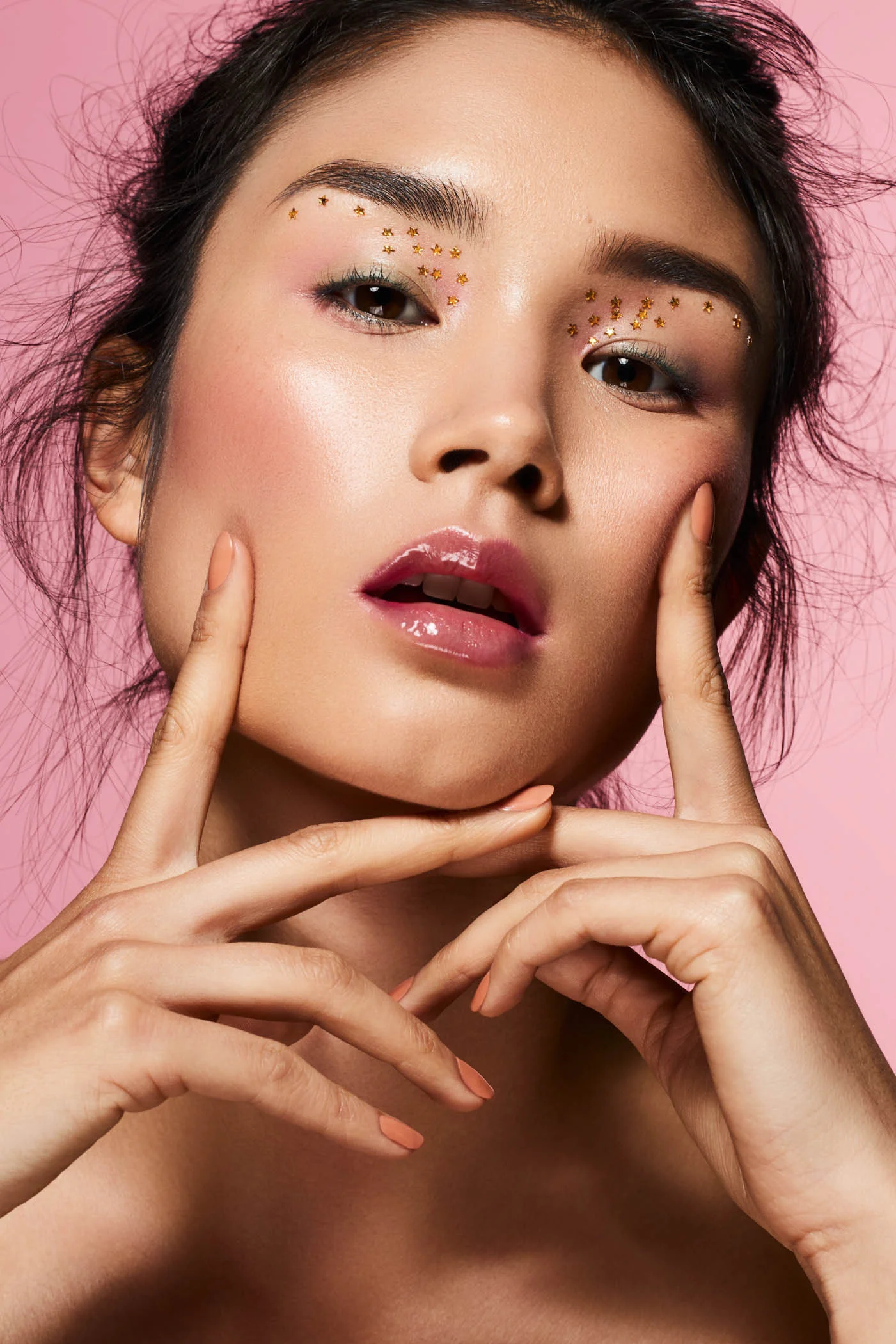 Asian beauty model with gold star eye makeup in front of a pink studio backdrop