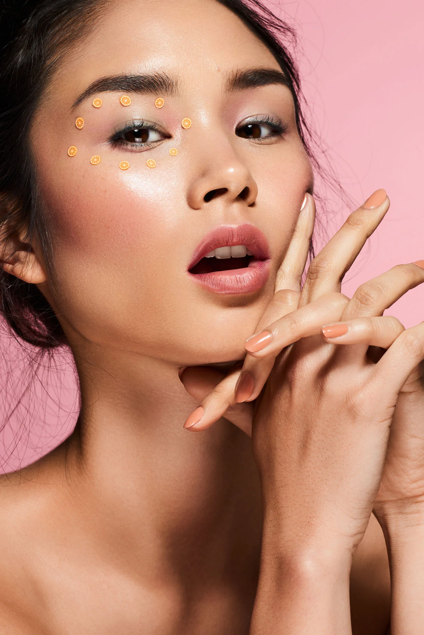 Asian beauty model with orange fruit stickers in front of a pink studio backdrop