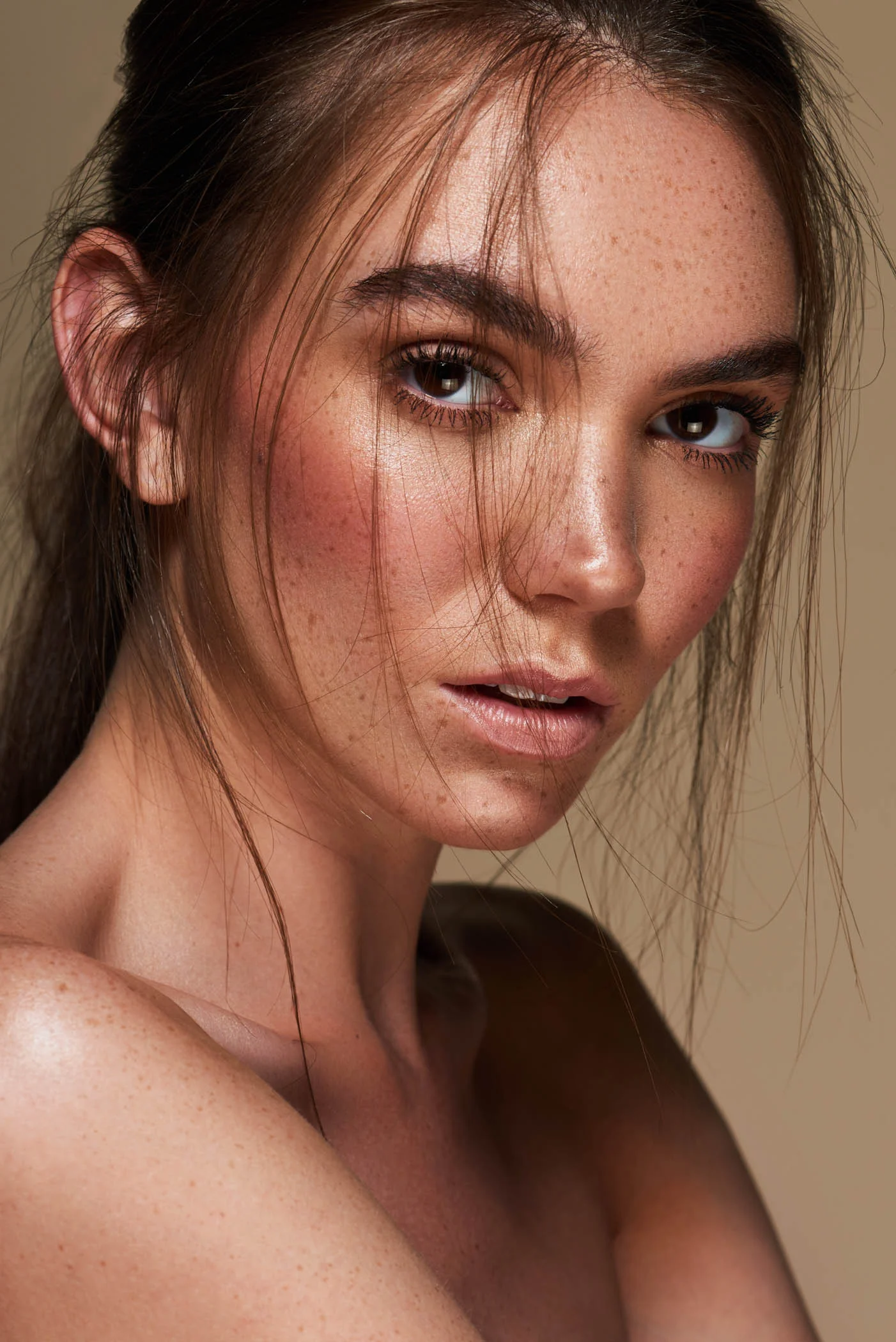 Freckled female model with metallic makeup in front of a cream studio backdrop