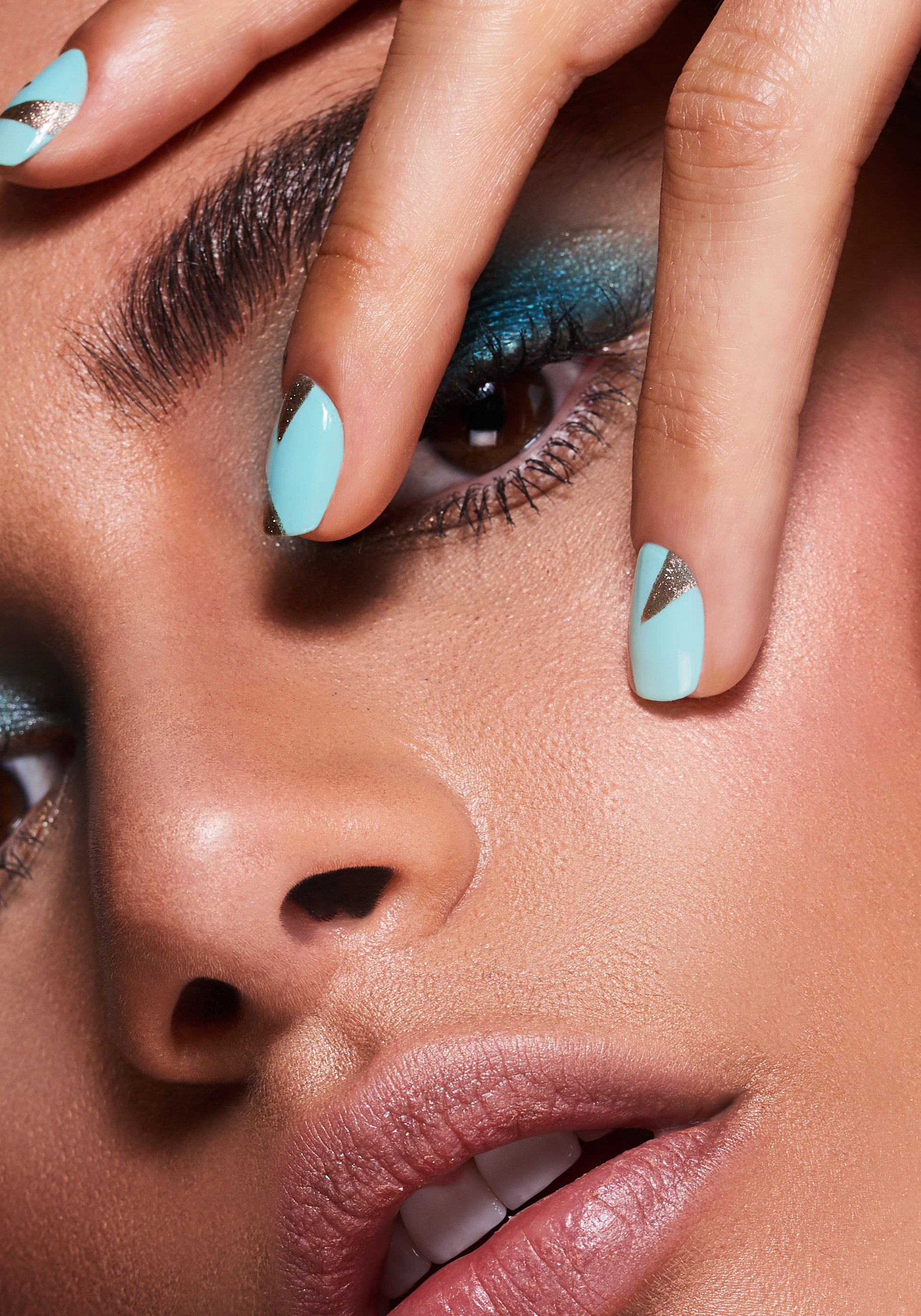 Macro close up of blue and gold nail art on a female beauty model with blue shimmer eyeshadow