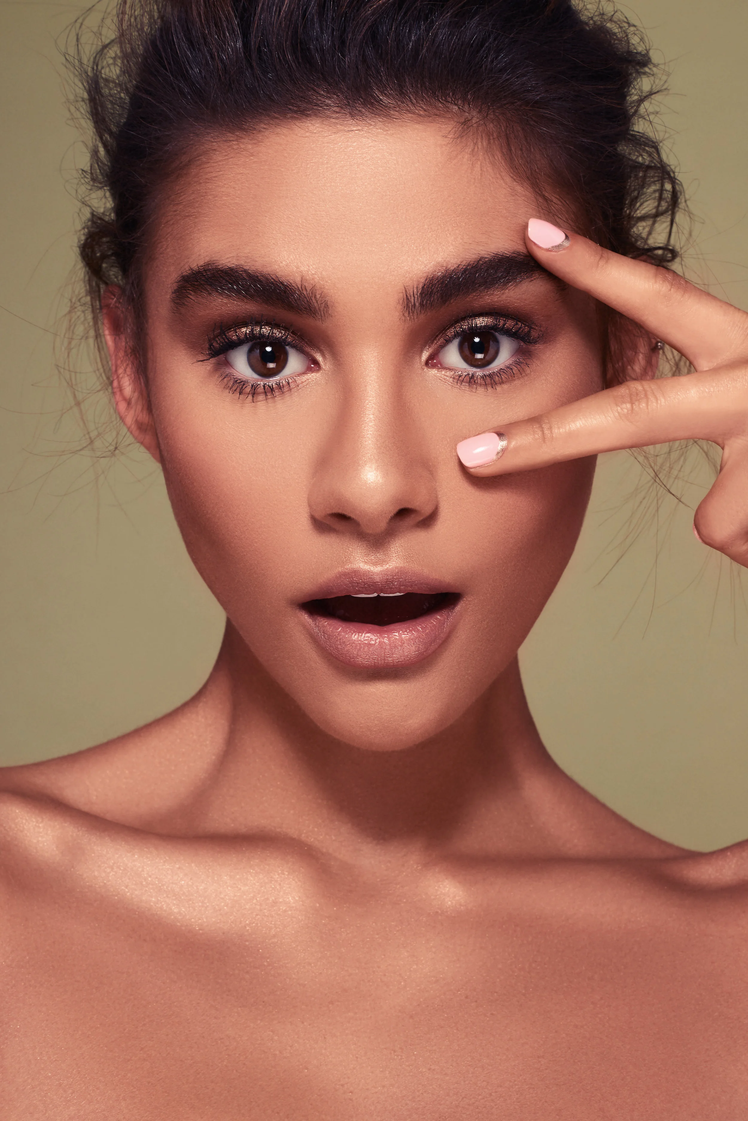 Tanned beauty model with flawless skin, gold eyeshadow and pink nail art