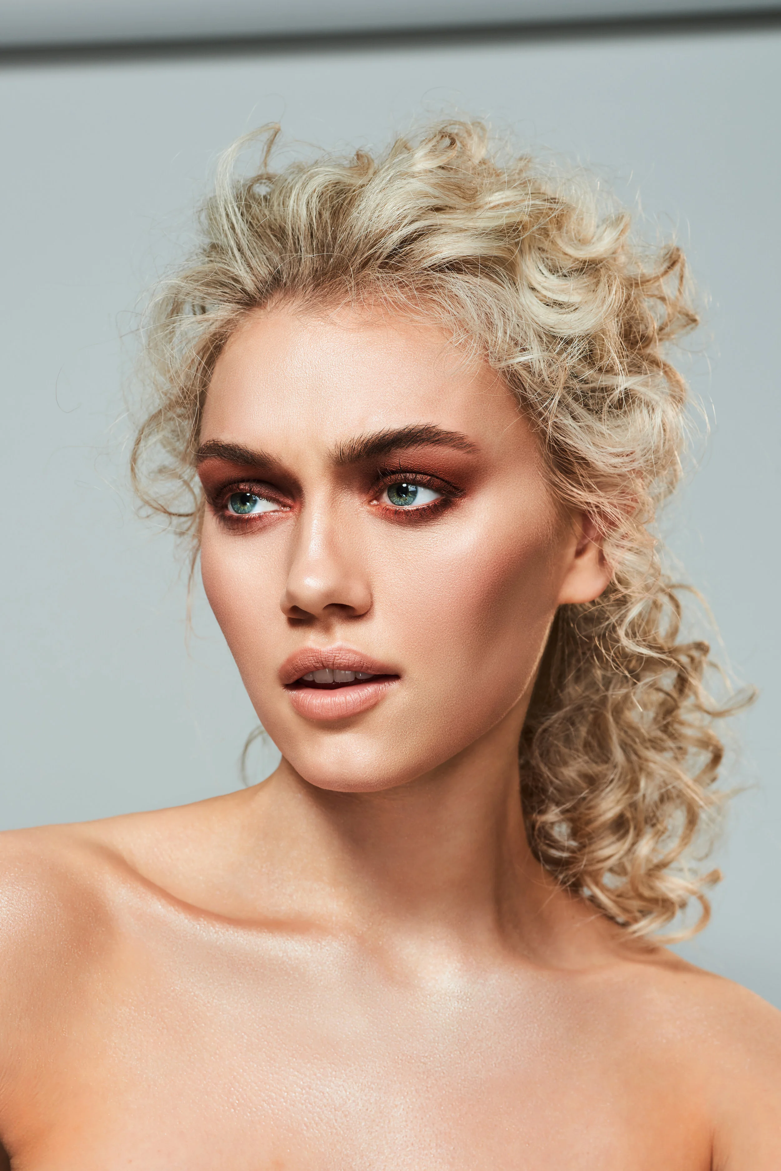 Blonde beauty model with curly permed hair and brown shimmer eyeshadow makeup