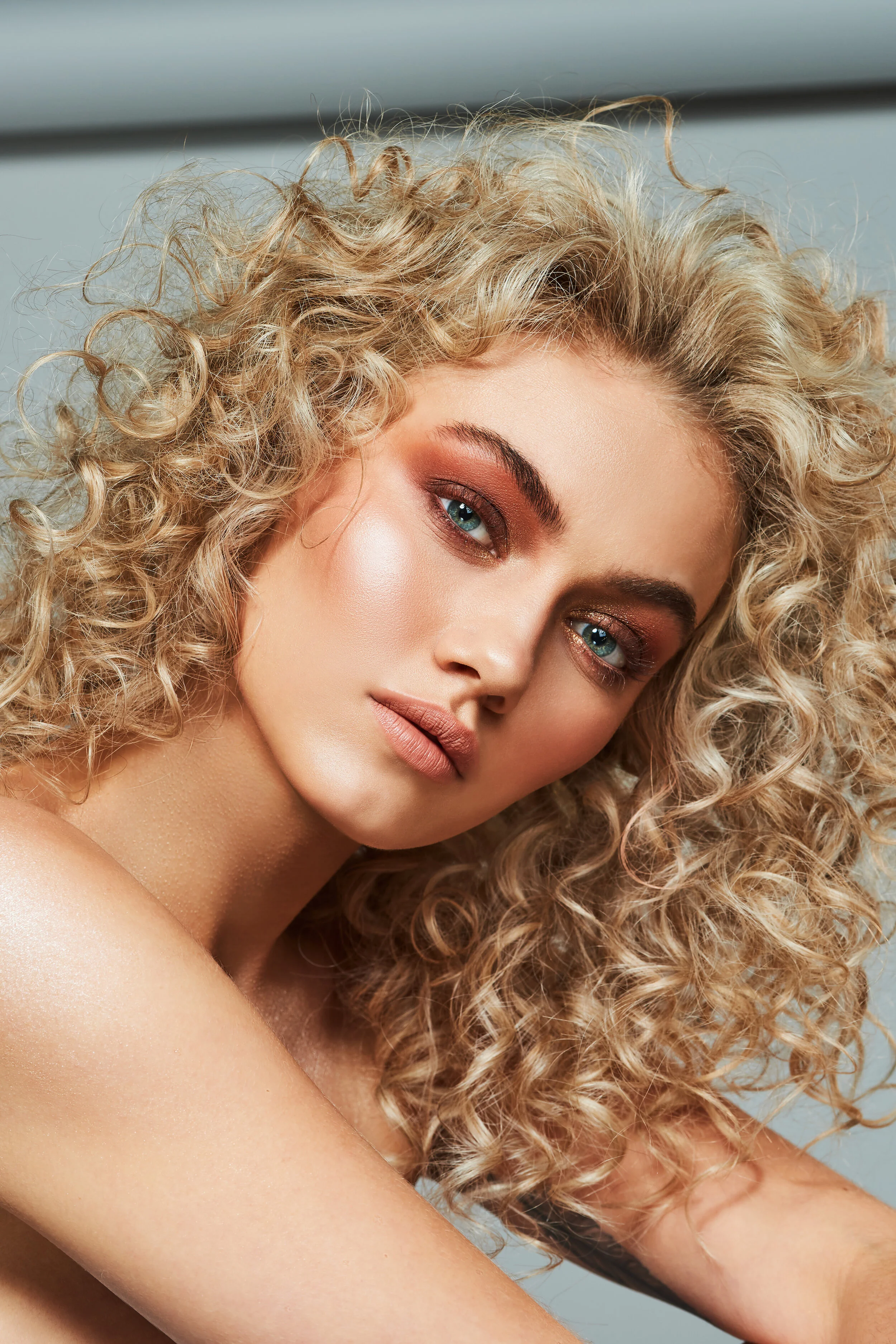 Blonde beauty model in front of grey backdrop with curly permed hair