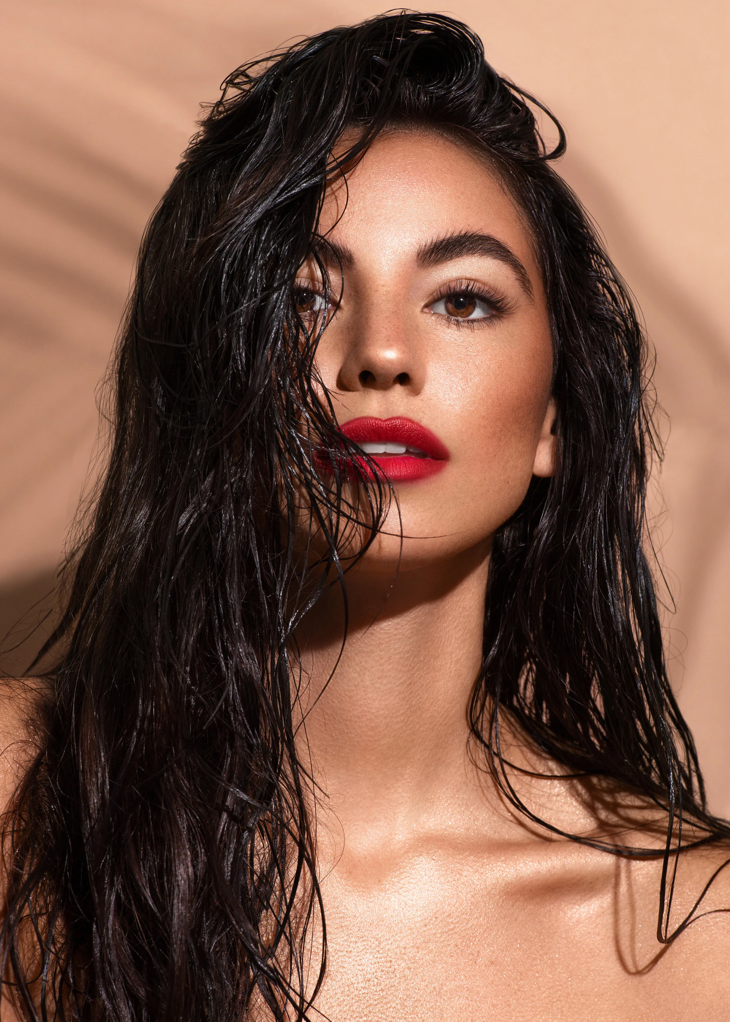 Tanned beauty model wearing red lipstick with wet messy hair in front of nude studio backdrop
