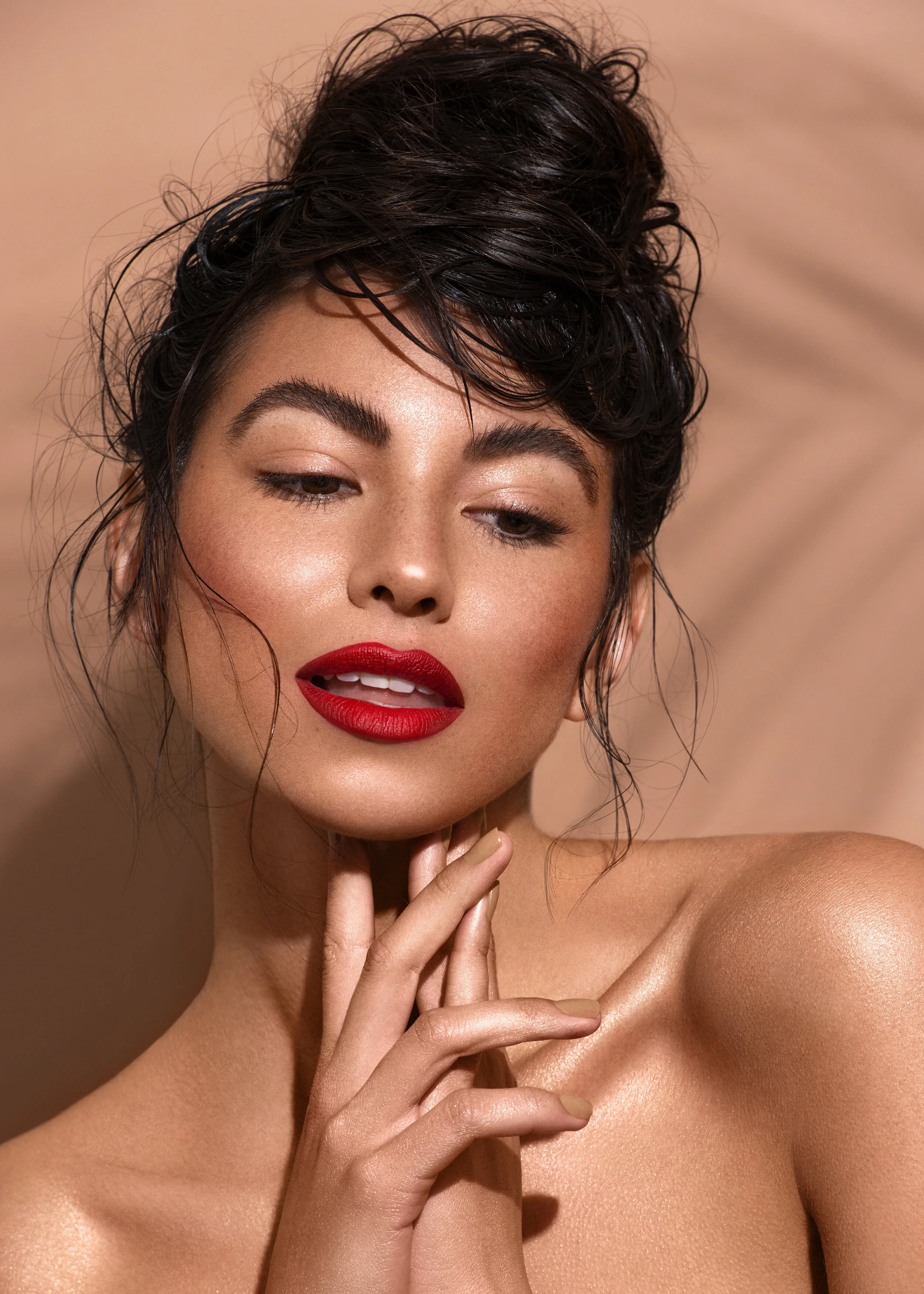 Tanned beauty model wearing red lipstick in front of nude backdrop with palm leaf shadow