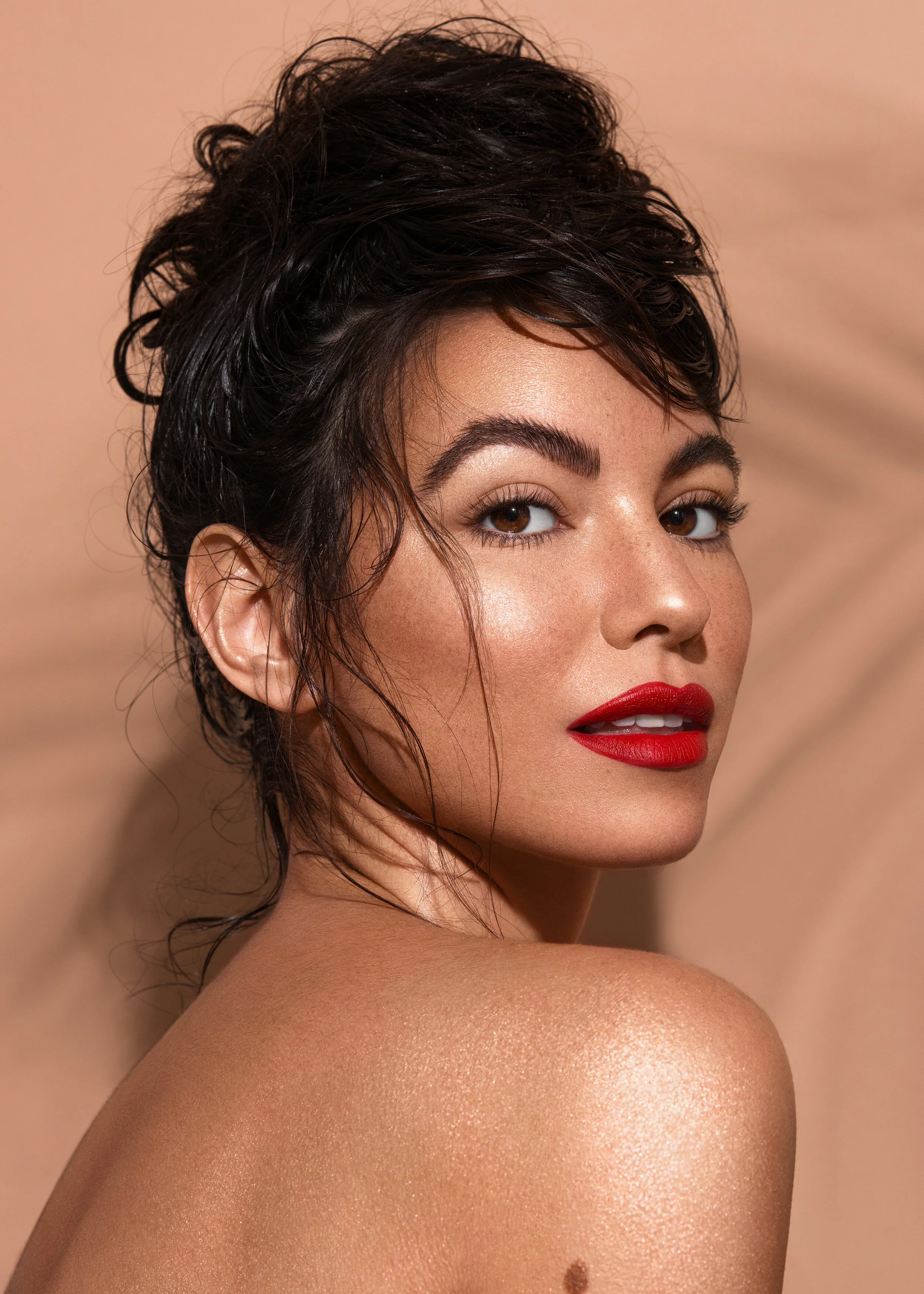 Tanned beauty model wearing red lipstick in front of nude backdrop with palm leaf shadow