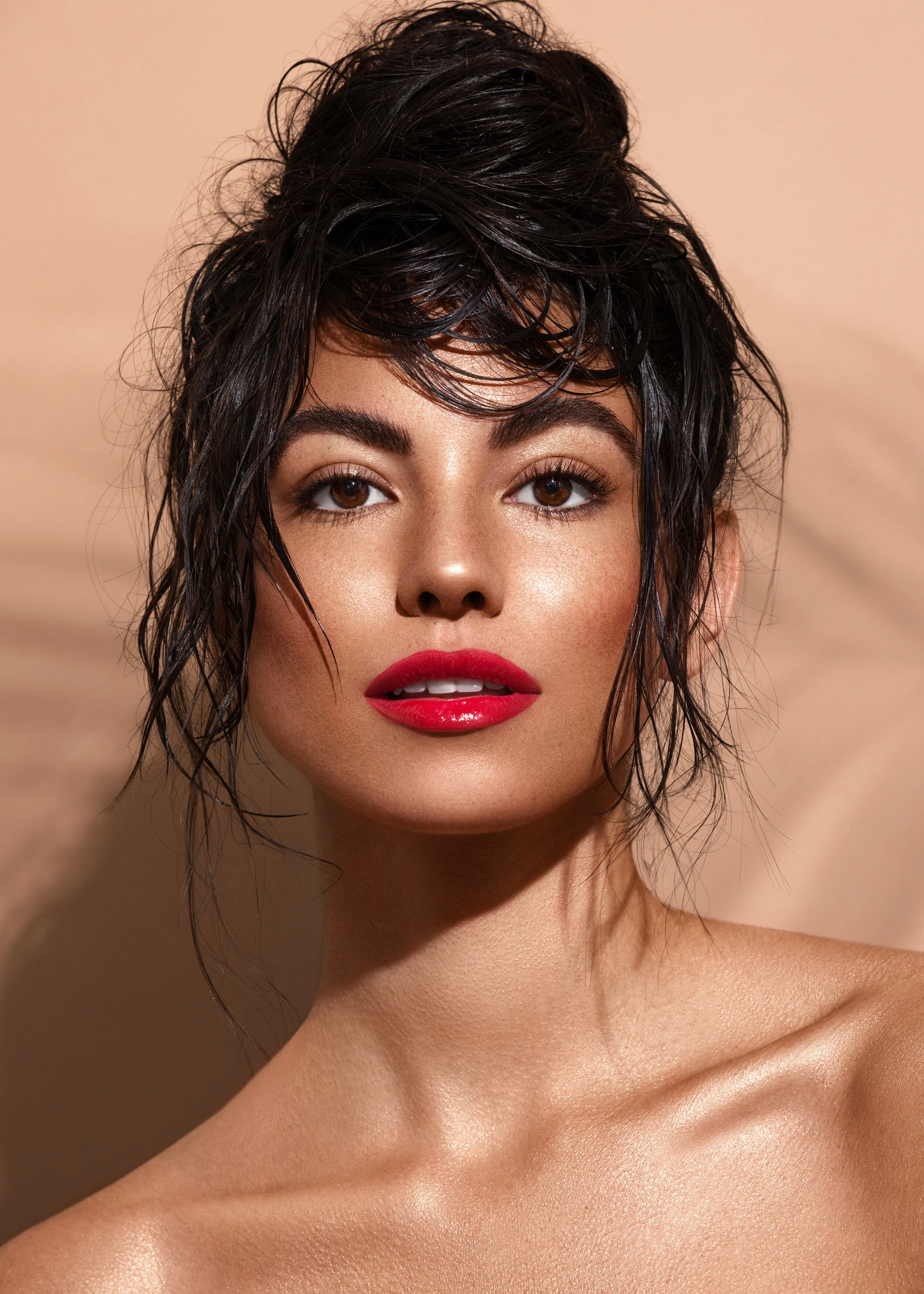 Tanned beauty model wearing red lipstick with wet messy hair in front of nude studio backdrop