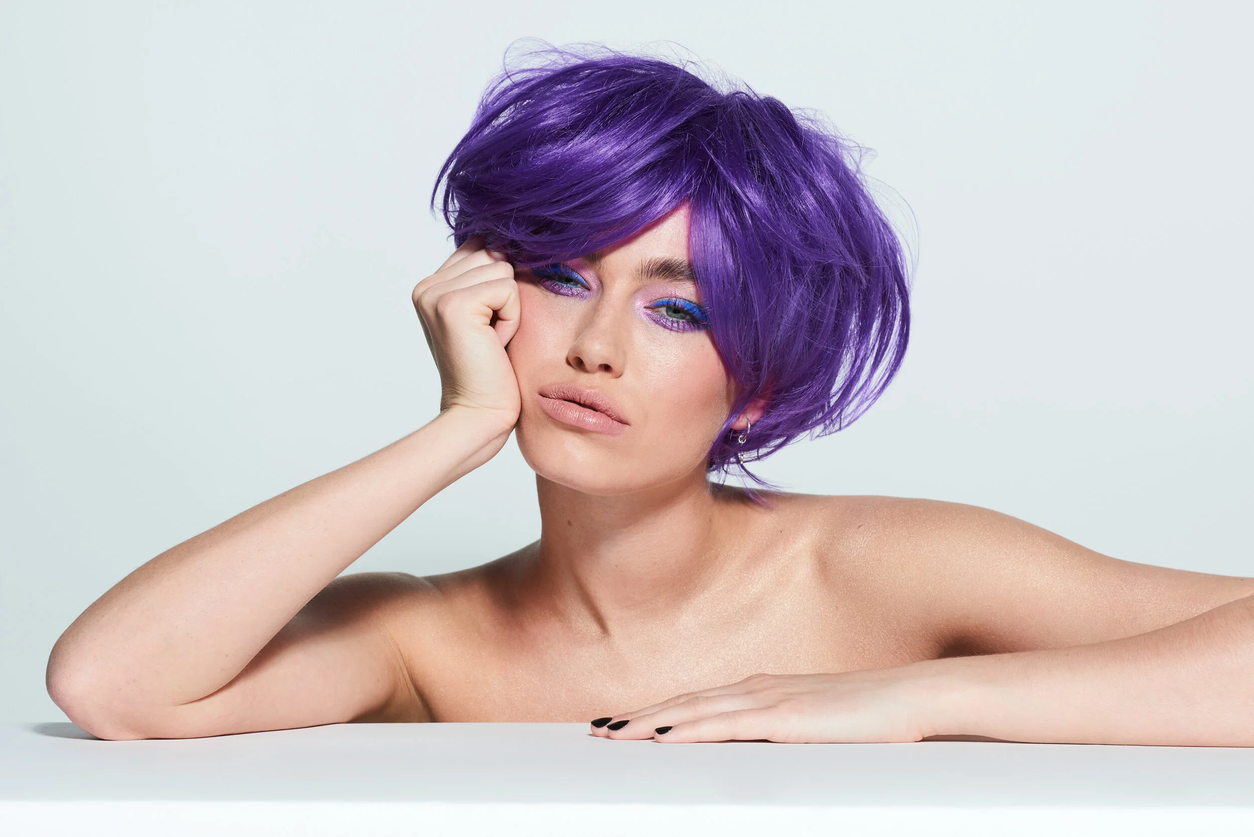 Female beauty model wearing a purple wig for LGBT Hair shoot on white backdrop