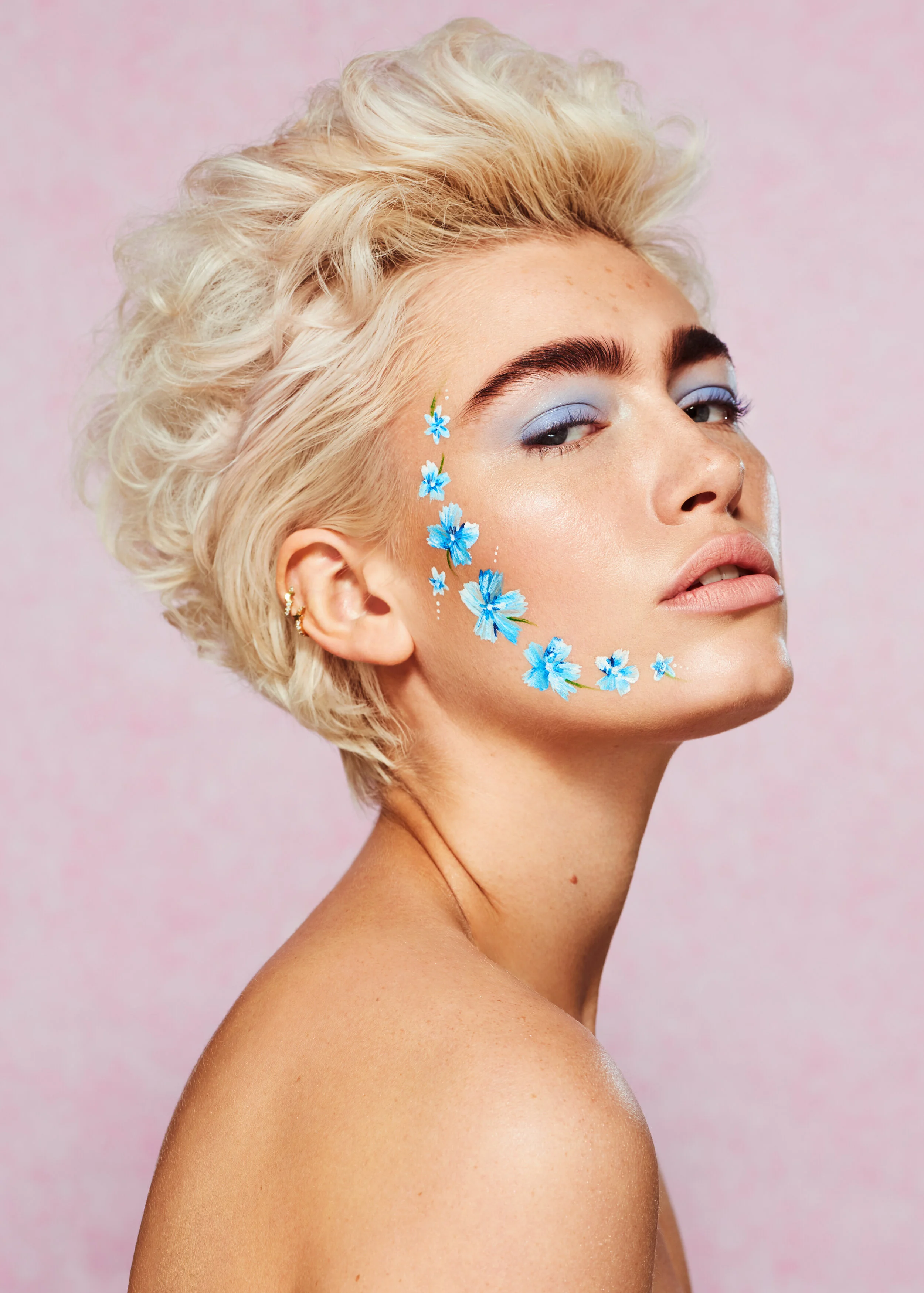 female model with short curly blonde hair and blue flower face paint art