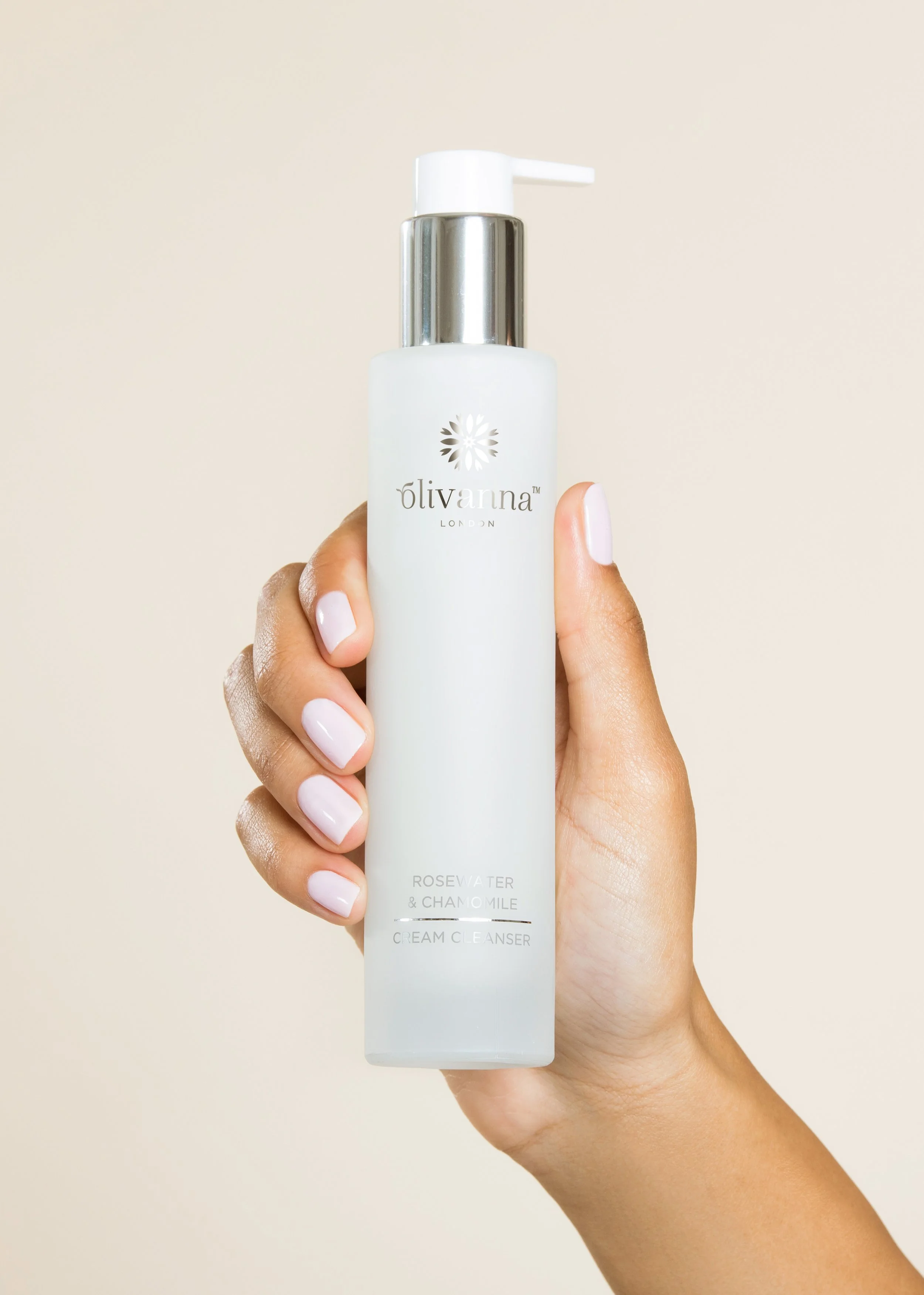 Womens hand holding Olivanna skincare bottle in front of beige studio backdrop