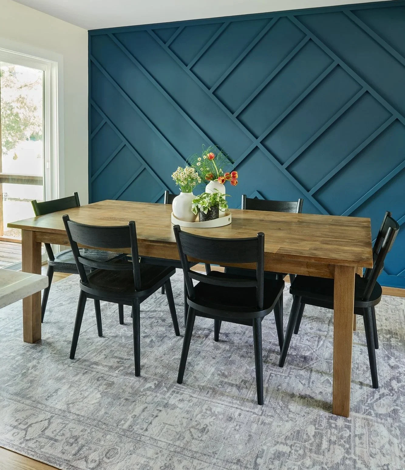 Dining room with custom, bold geometric accent wall painted in a dark teal tone. There's a wood dining table with black chairs in front of it.