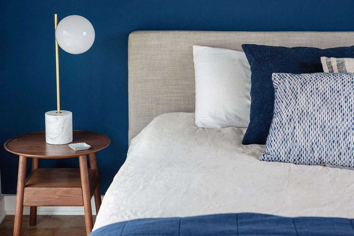 Bedroom with blue walls, light bed and walnut nightstand.