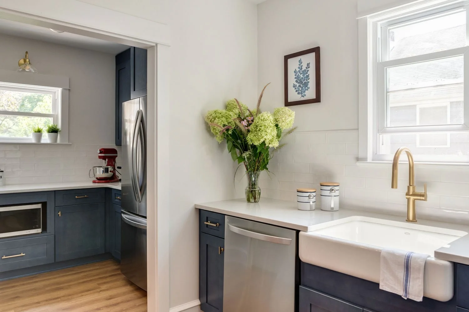 View into an open kitchen pantry that has additional counter space, a microwave, KitchenAid mixer and refrigerator.