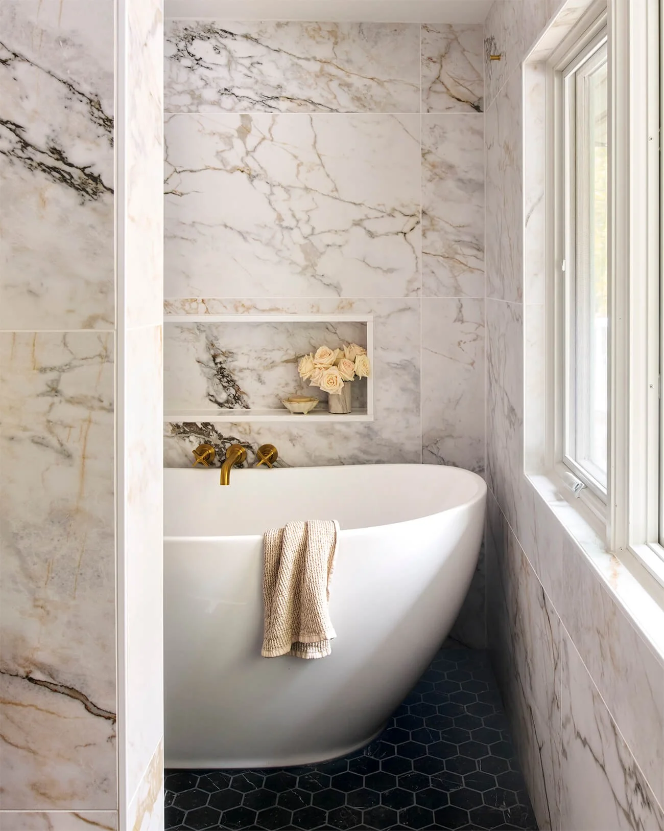 White curved freestanding tub in front of window.