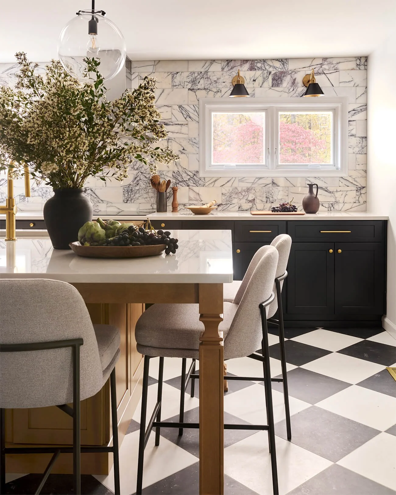 Wood kitchen island in front of black perimeter cabinetry. Black and white checkerboard tile floor.