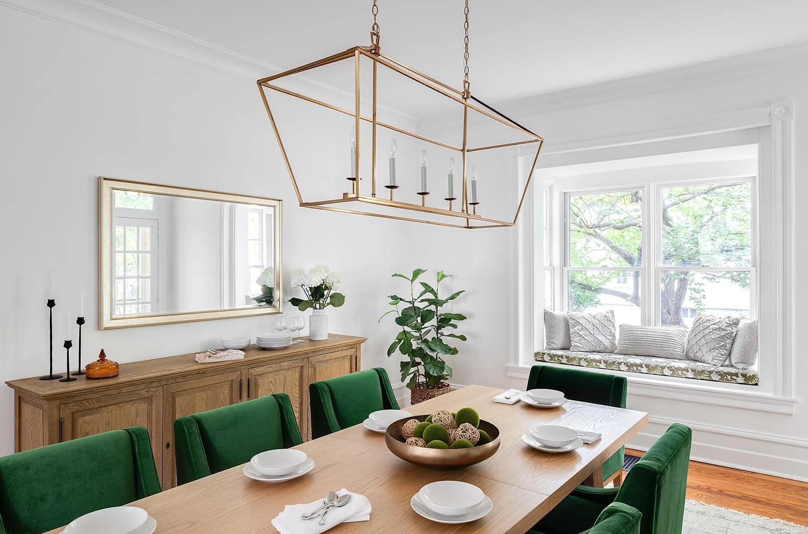 Large dining room with emerald green chairs and an oak table and side board.