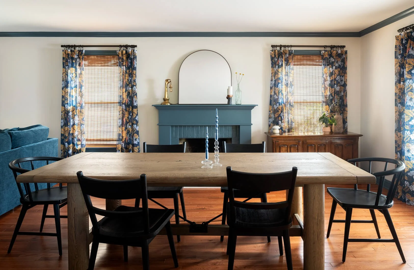 Large wood dining room table with black chairs in front of blue mantle.