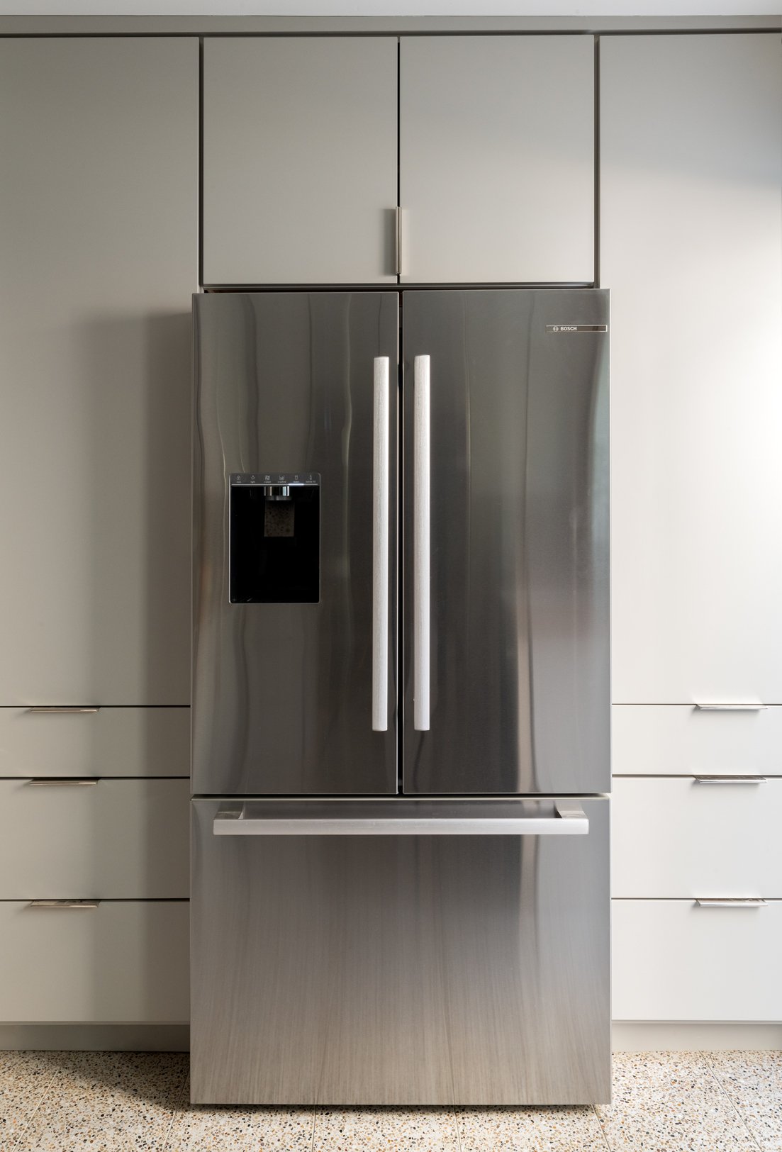 Refrigerator wall with light gray full height cabinetry surrounding it.