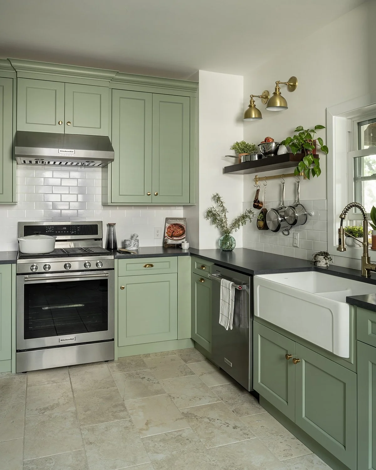 Small kitchen with sage green cabinetry, white subway tile and travertine look floor tile.