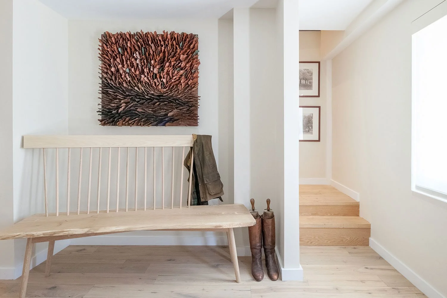 Warm white foyer with oak floors and a custom made bench with artwork above.