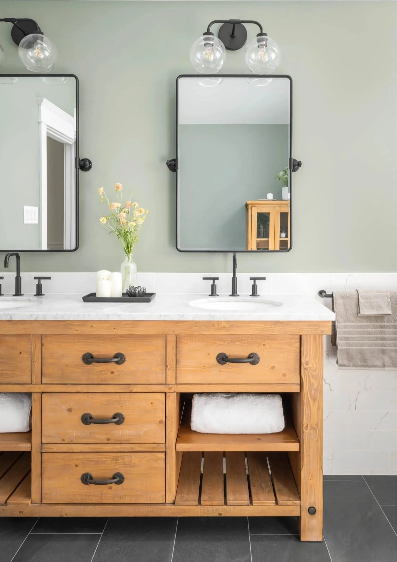 Rustic wood vanity in front of a marble-look tile wainscot with sage green paint above.