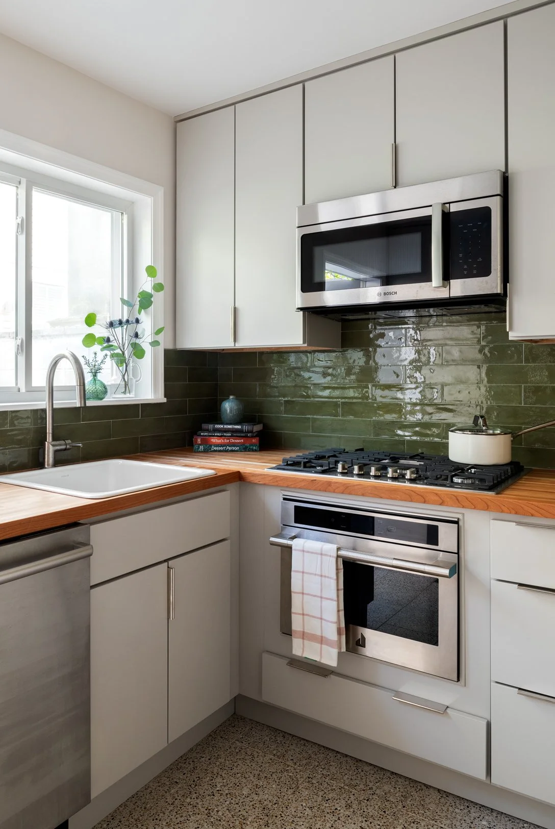 Kitchen with light gray cabinetry, butcher block countertops and a dark green backsplash.