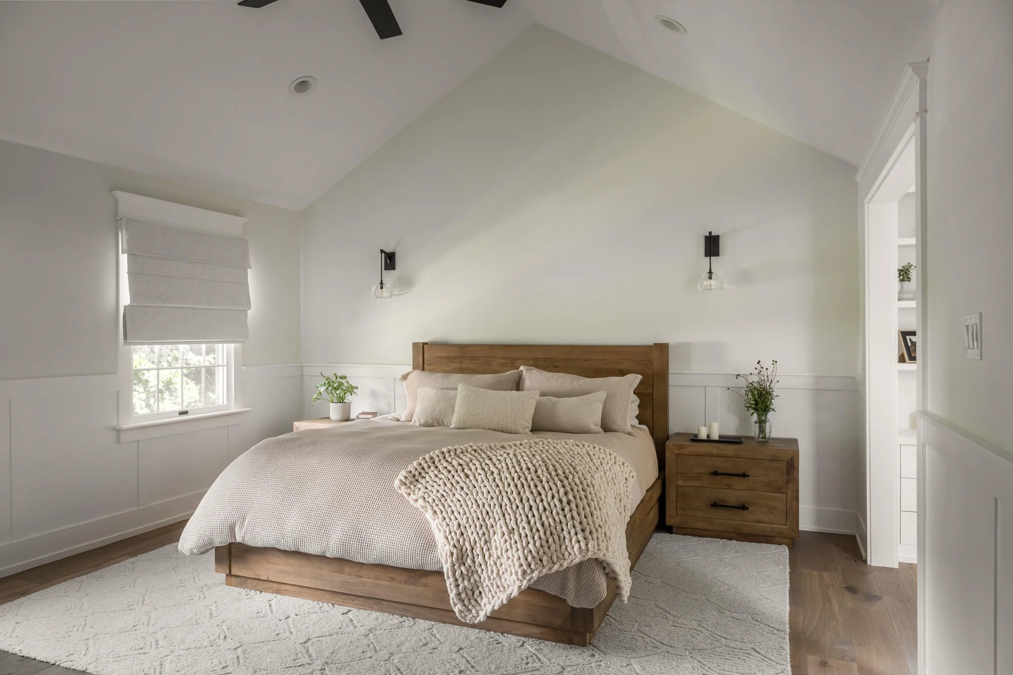 Primary Bedroom with white wainscot and a wide plank wood floor. All the furniture is rustic wood on an beige rug.
