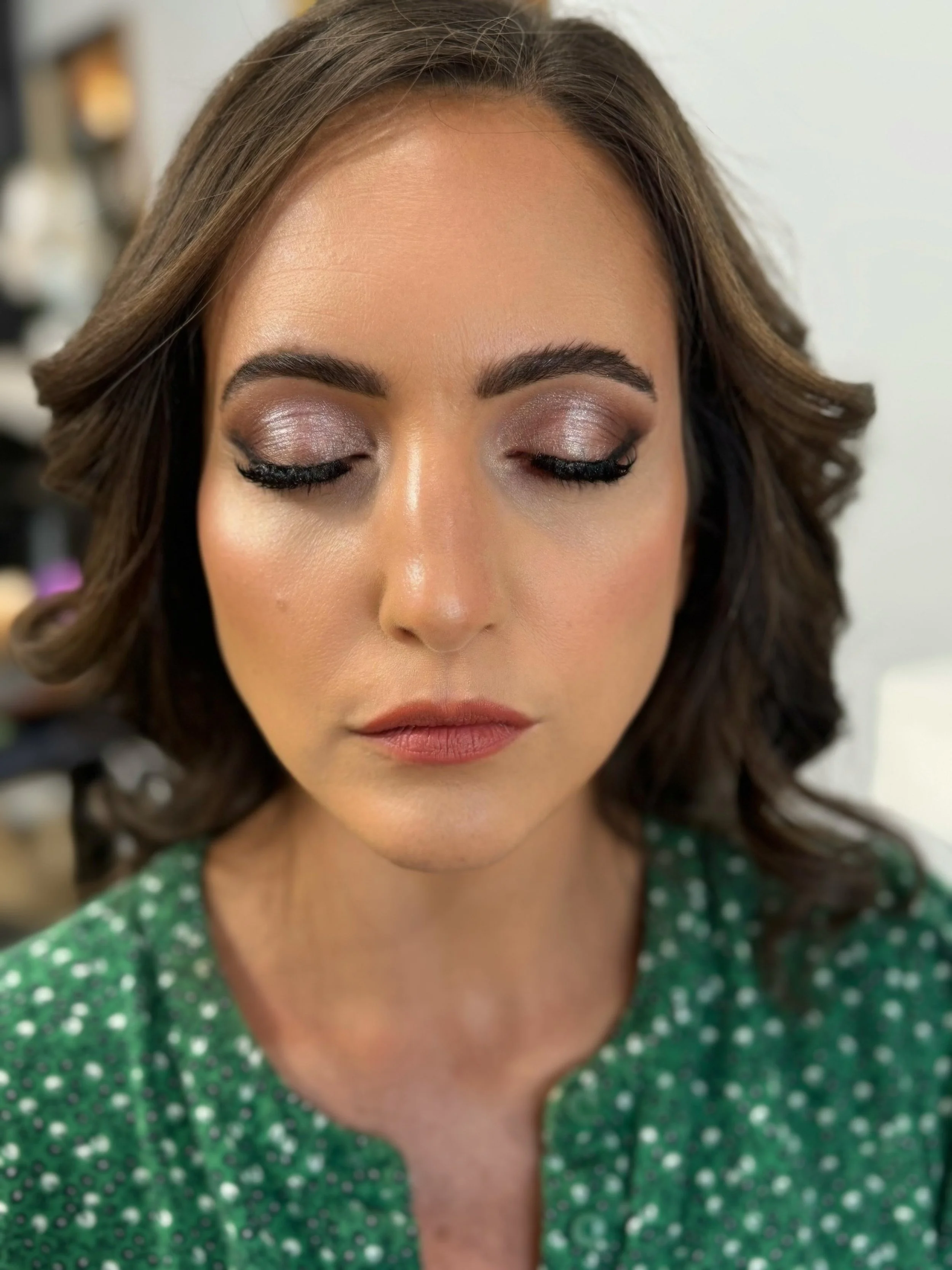 Close-up of a woman with closed eyes, makeup applied, wearing a green dress with white polka dots.