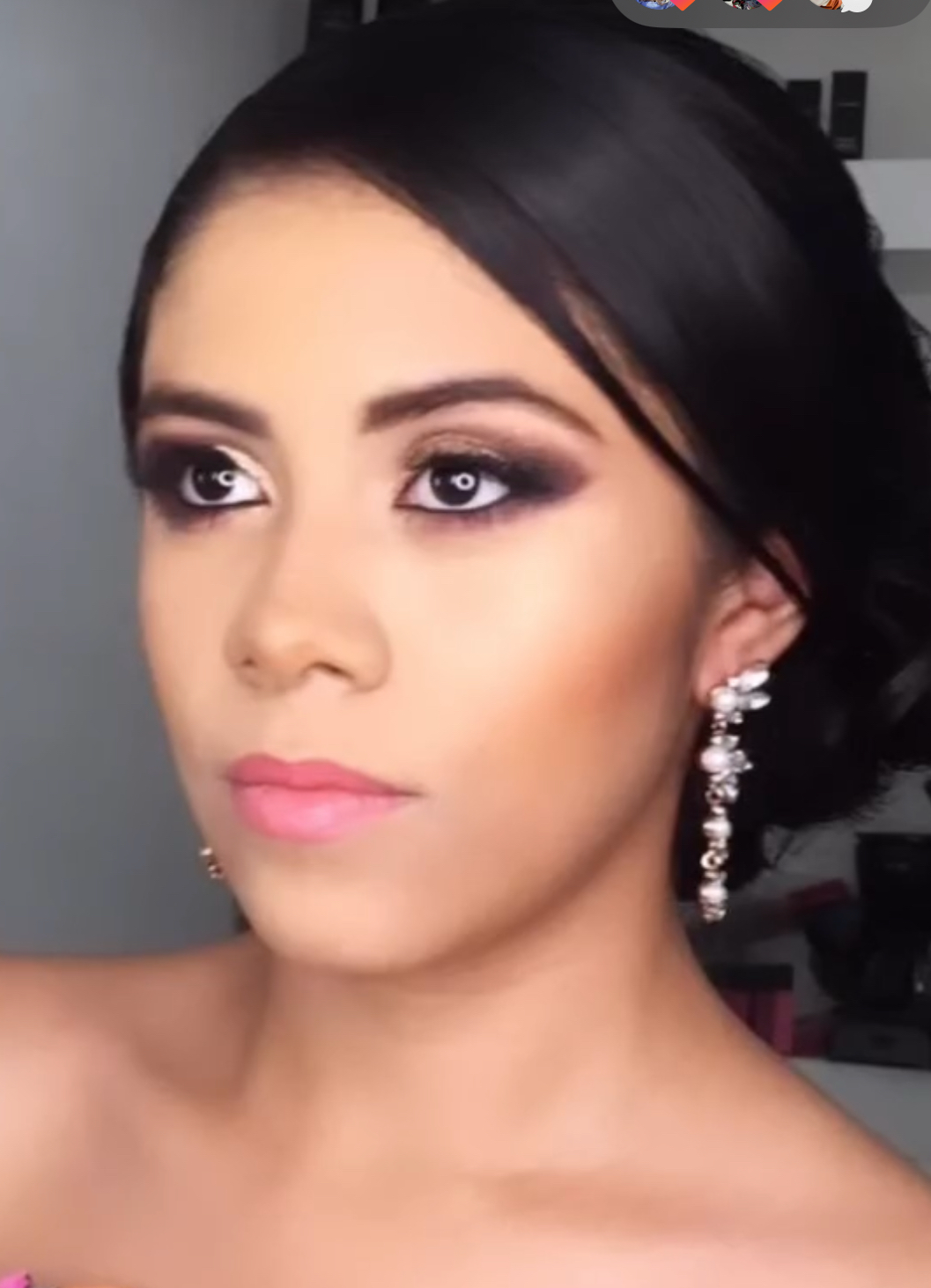 A woman with styled black hair and makeup, wearing large pearl and crystal earrings, looking slightly off-camera.