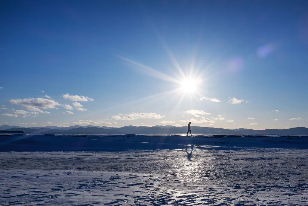 "The Long Walk Back" March 2014, Burlington, Vermont Fujifilm X100s, 23mm, f/16, 1/320, ISO 200 When we checked into our hotel in Burlington, the concierge suggested we take a walk across the frozen Lake Champlain. This seemed like a terrible and dangerous idea. But sure enough, people were out there traipsing around all over the ice. So we took a walk on the lake. After all, "when in Rome." Sure enough, it was frozen solid, clear across to New York. This is the first time the winter has been cold enough for the lake to freeze since 2007. 