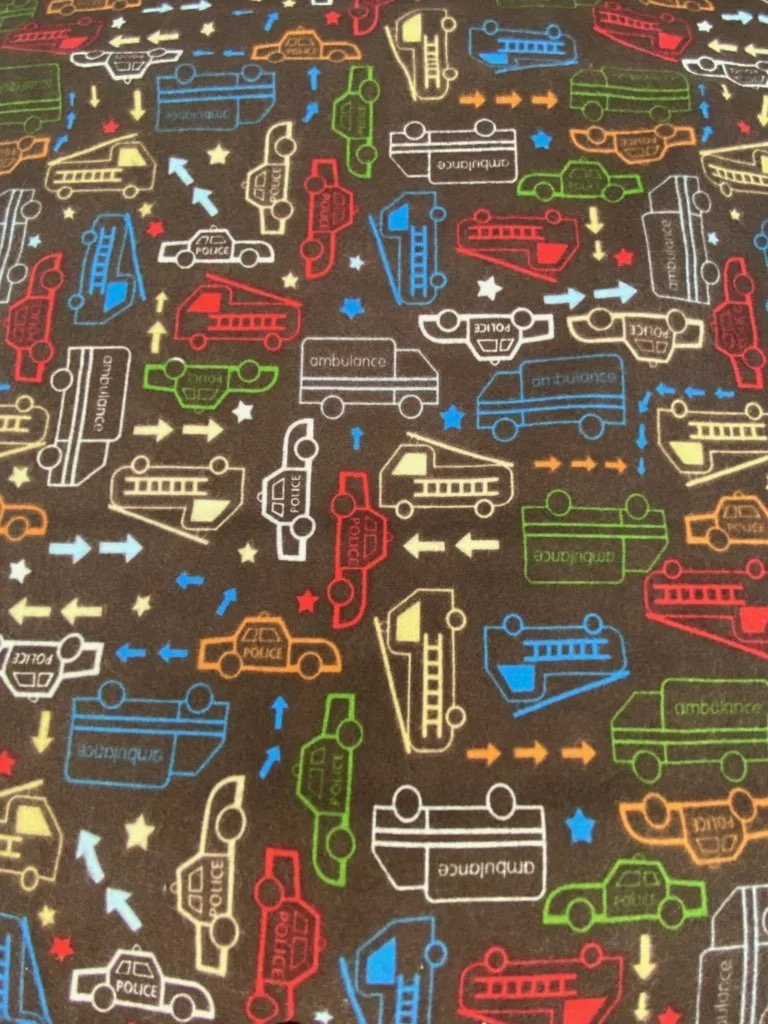 Cotton flannel fabric by Hoffman Fabrics features first responder vehicles and trucks in fun primary colors on a brown background.
