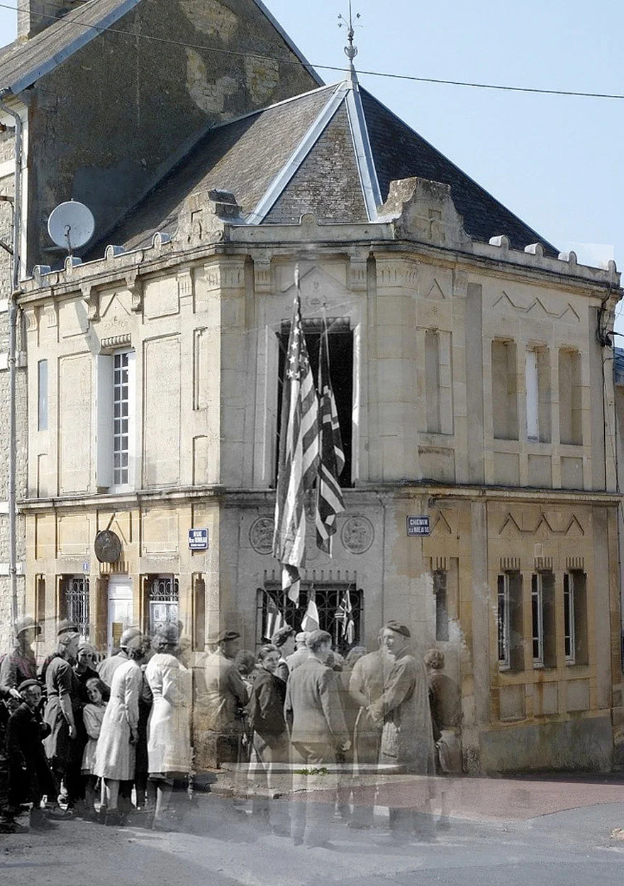 “A group of civilians and GI’s in front of the notary office of Trévières Street Octave Mirbeau. The entrance is decorated with French and allied flags.”
