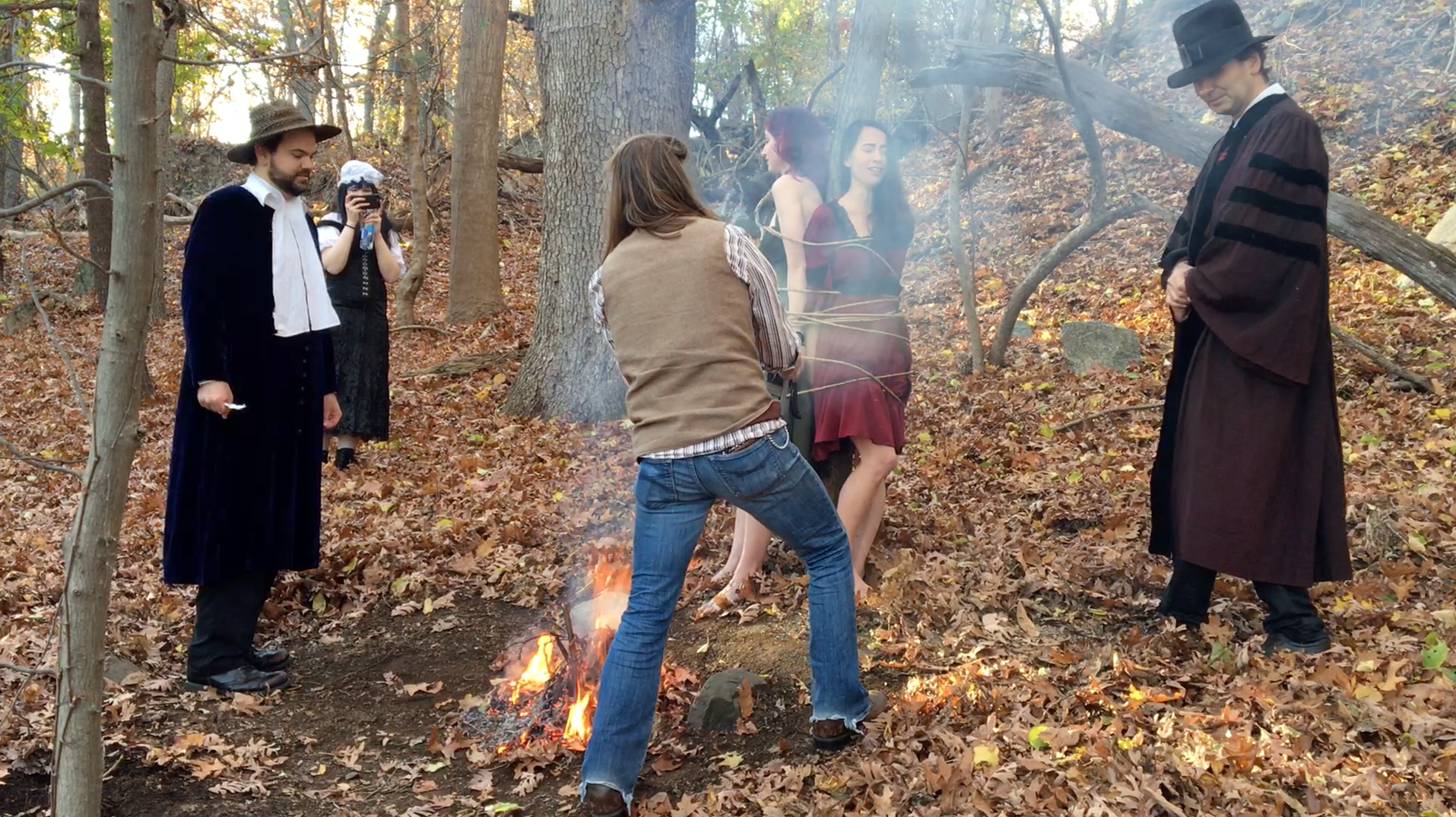 John Hartman of Reel Groovy Films on camera captures witches Geena Matuson (@geenamatuson) and Maya Simone burning at the stake. At back, Eve Xastur takes some photos while pilgrims Dawn Nightshade and Caleb Huntington bear witness.